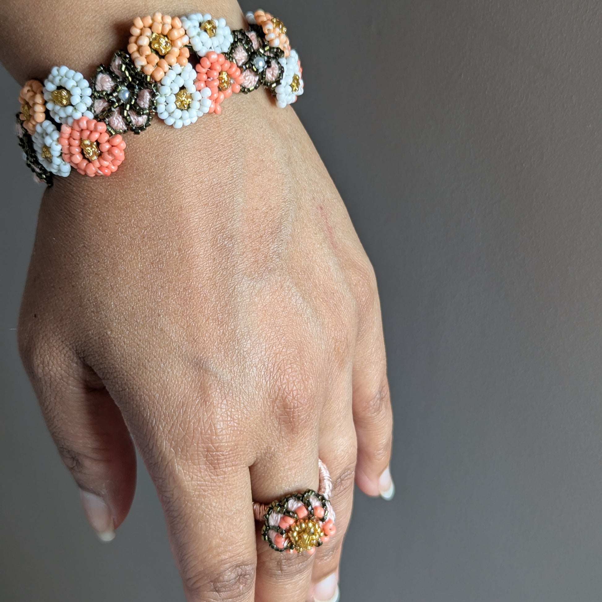 Close up of a hand wearing the Padmika 5-in-1 separate wrist bracelet and ring elements against a neutral grey backdrop.