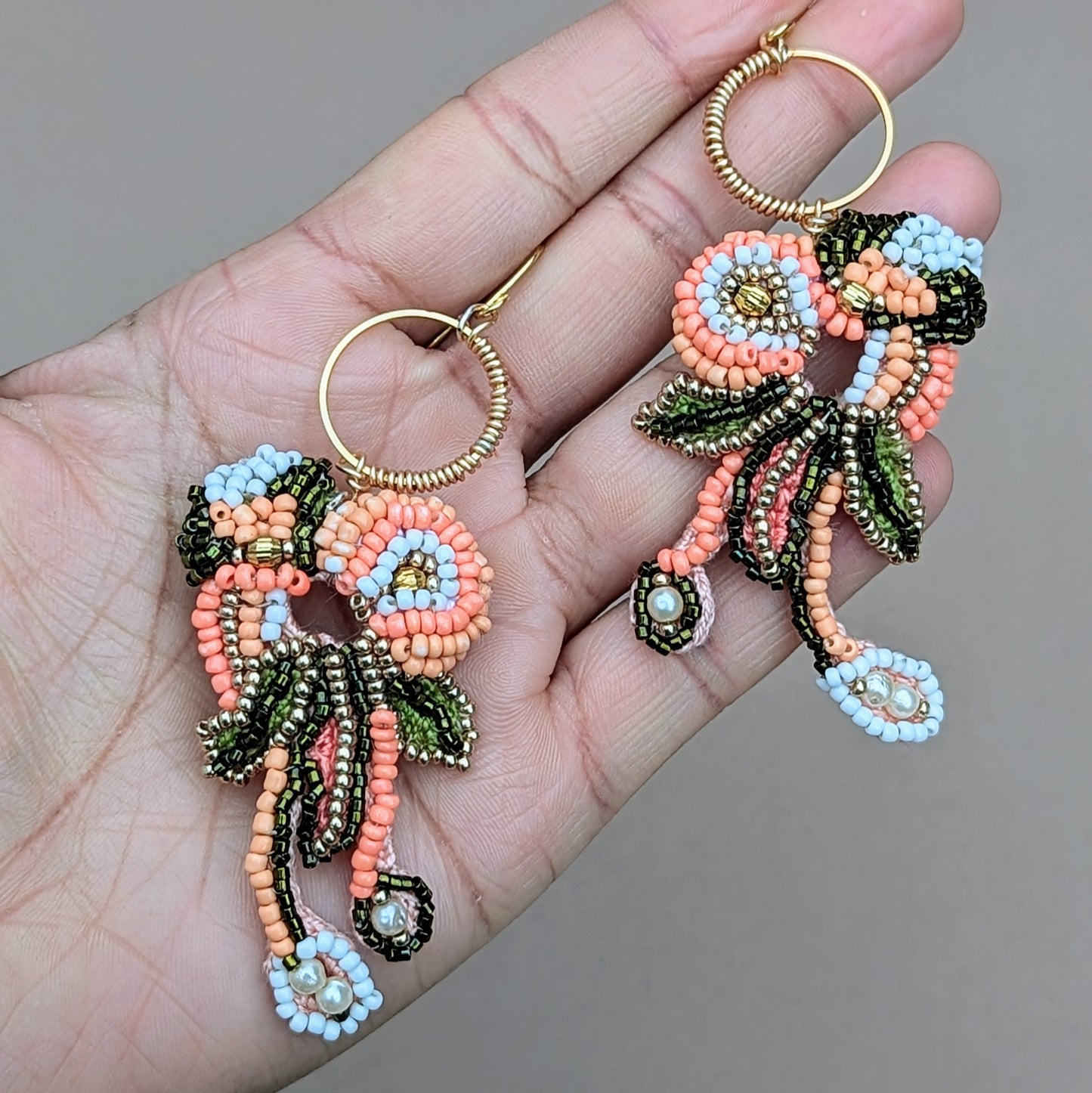 Close-up of Padmika handmade Indian earrings showing peach, green and gold beadwork, crochet detailing and dangling glass bead accents.