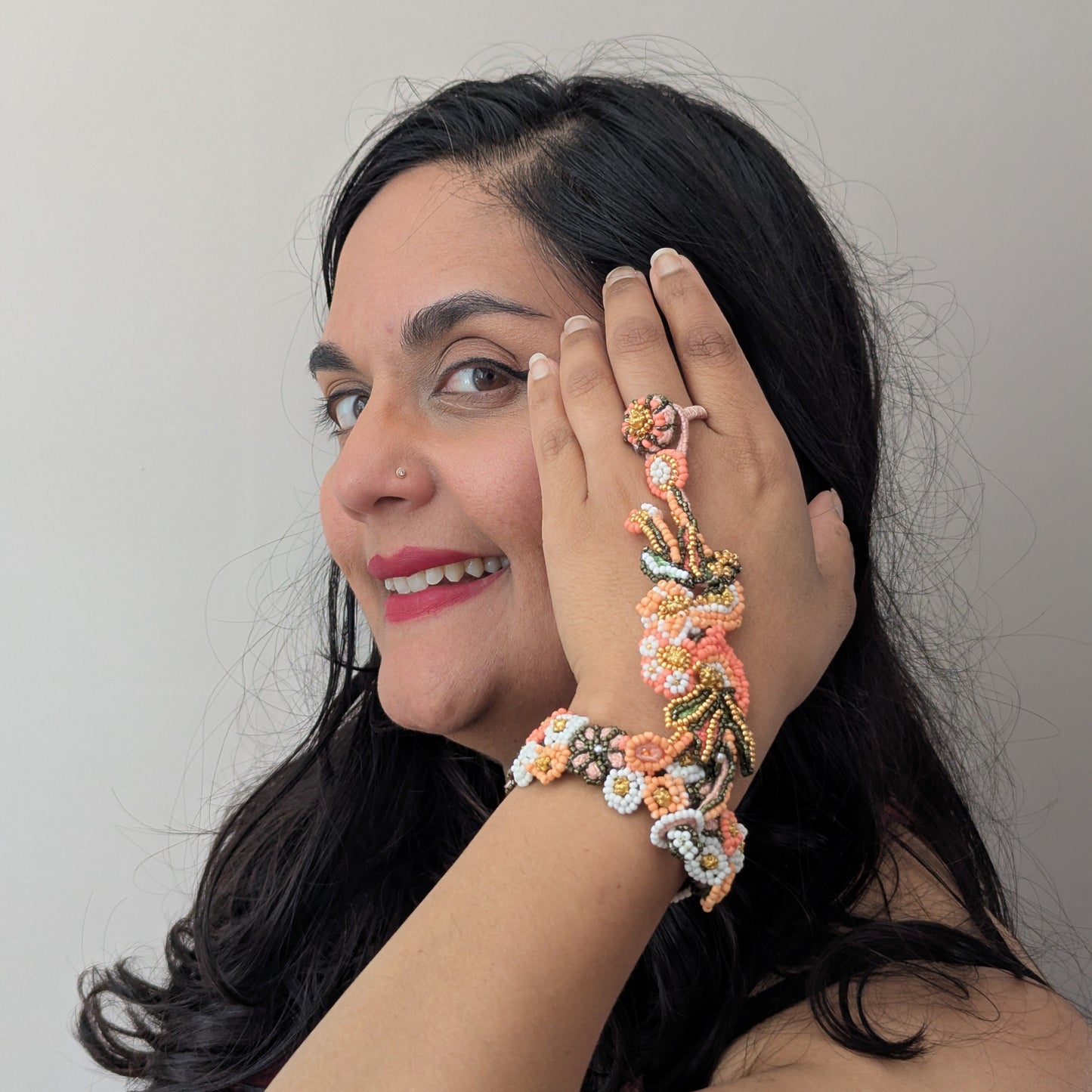 Mayaani UK artisan Megha modelling the Padmika 5-in-1 Indian haath phool worn here as one full piece featuring intricate seed bead artistry in peach, orange and white with green and gold accents.