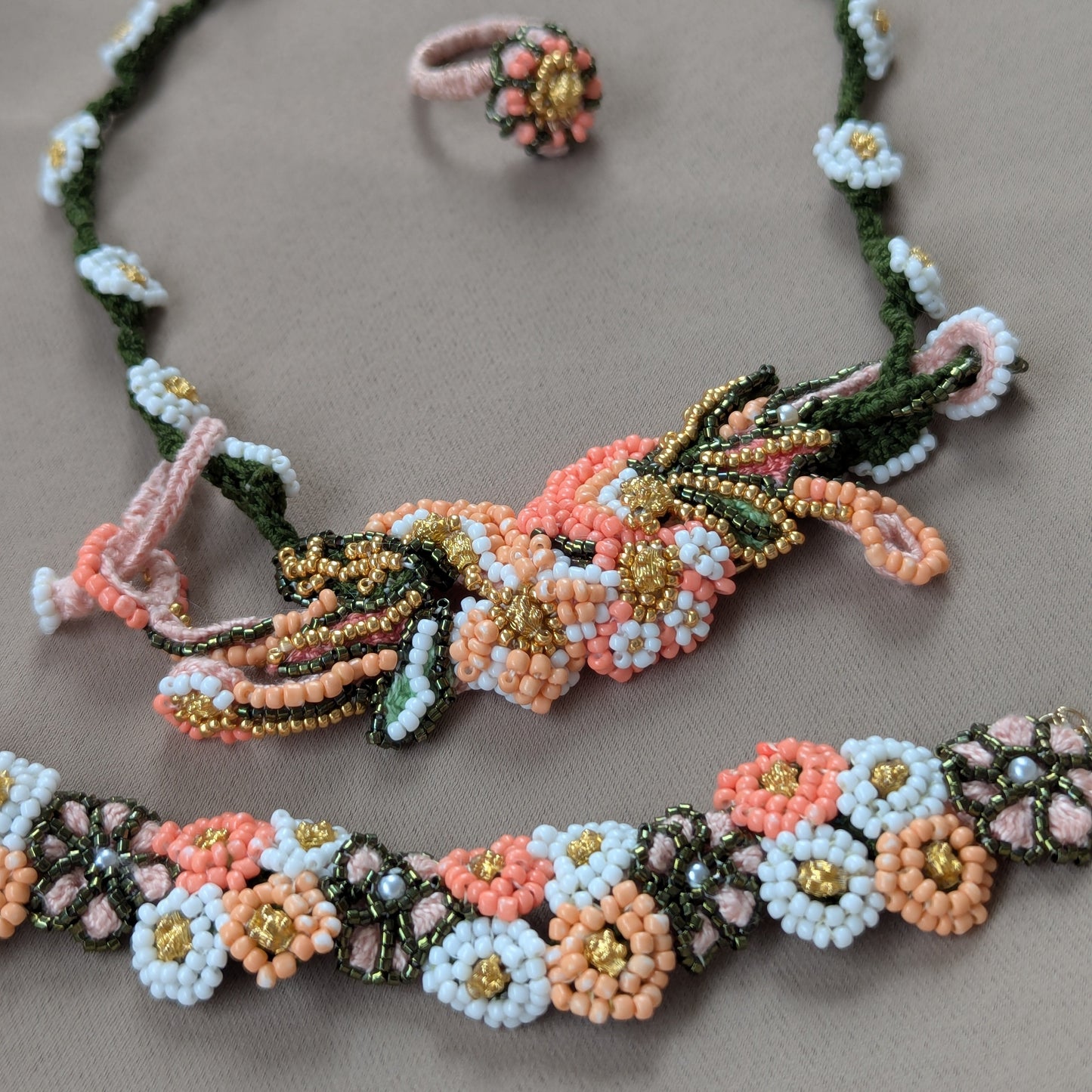Close up view of the Padmika 5-in-1 Indian bracelet necklace, ring and Western style bracelet elements richly bead woven in peach, green and white with vintage gold bead accents.