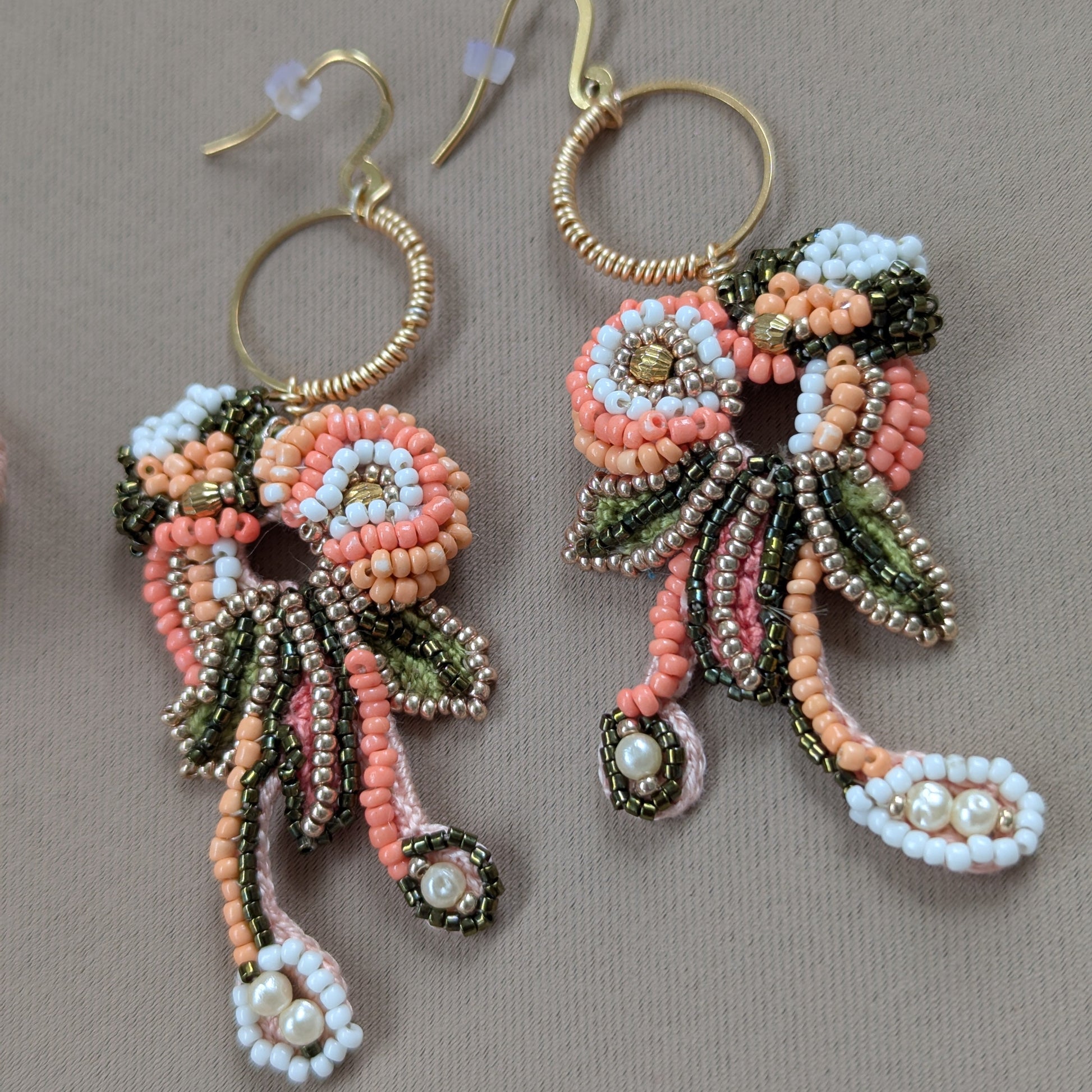 Close up flat lay view of the Padmika statement Indian chandelier style earrings intricately beaded in peach, green and gold.