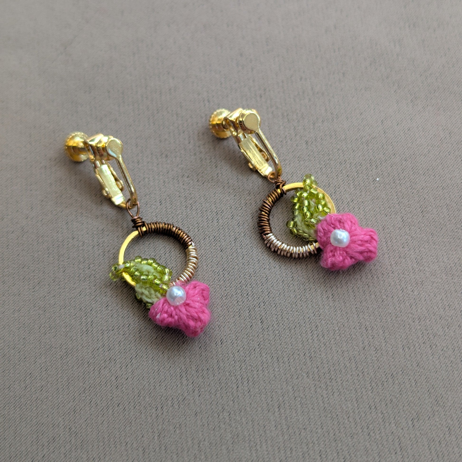 A handmade pair of elegant luxurious clip-on earrings featuring pink floral motifs and chartreuse green, pearl, bronze and gold accents designed for non-pierced ears.