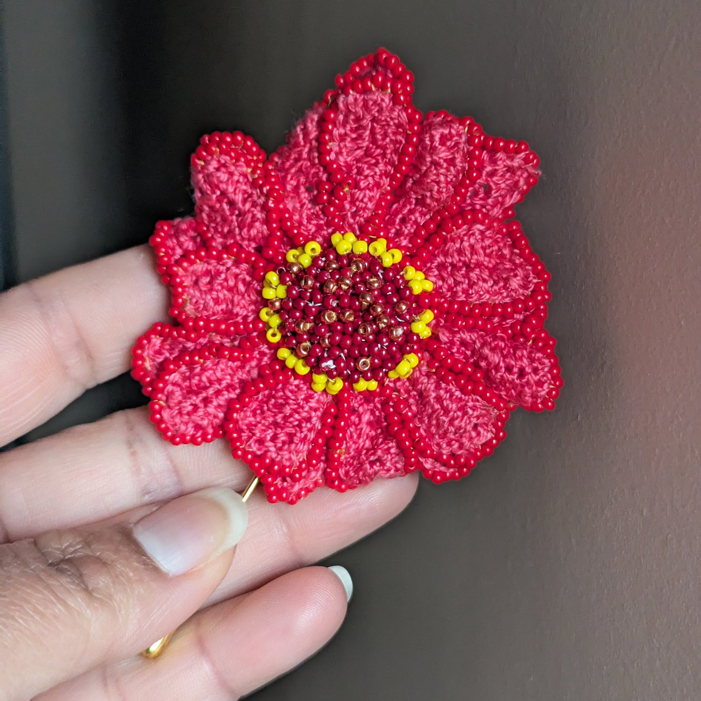 Hand held view of the Mayaani pink, yellow, red artisan hand woven bead crochet brooch designed and created as part of the garden of becoming Mayaani series.