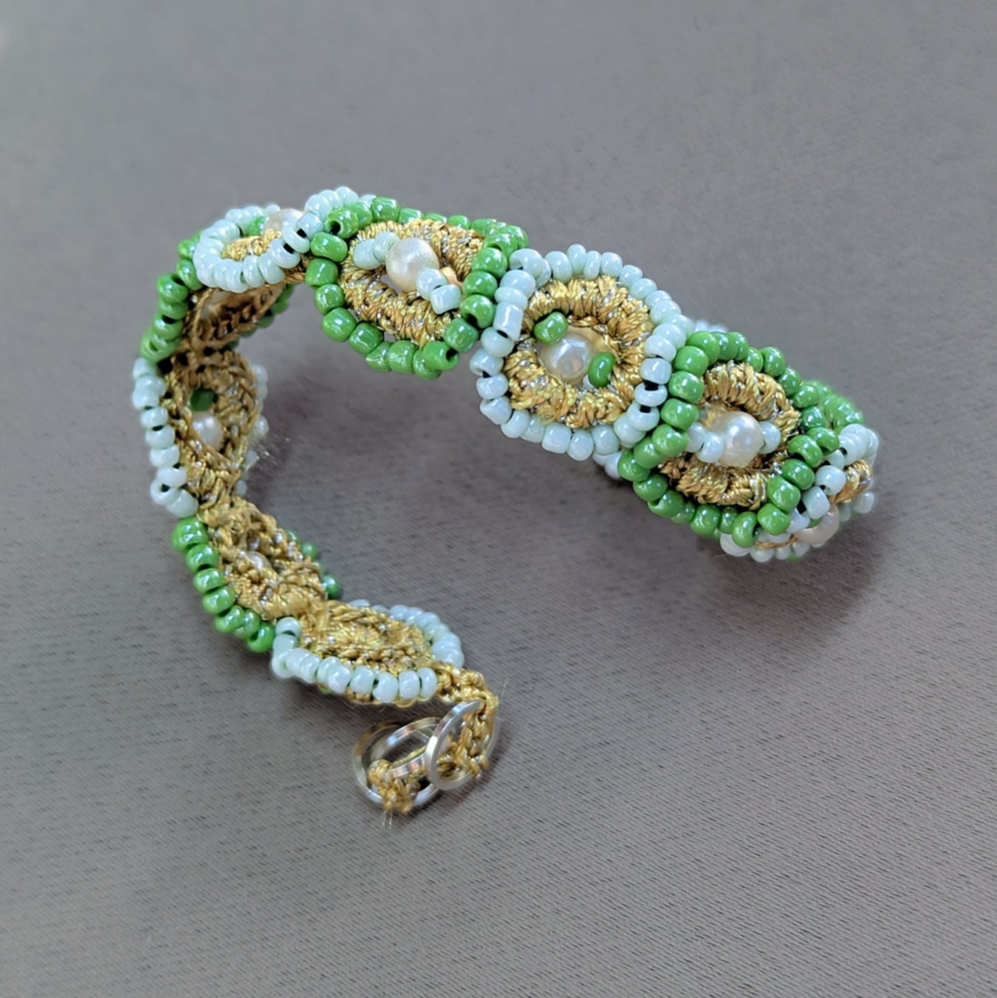 Close up view of a one of a kind statement beaded bracelet in gold and mint green and featuring vintage seed pearls handmade exclusively for Mayaani Jewellery UK.