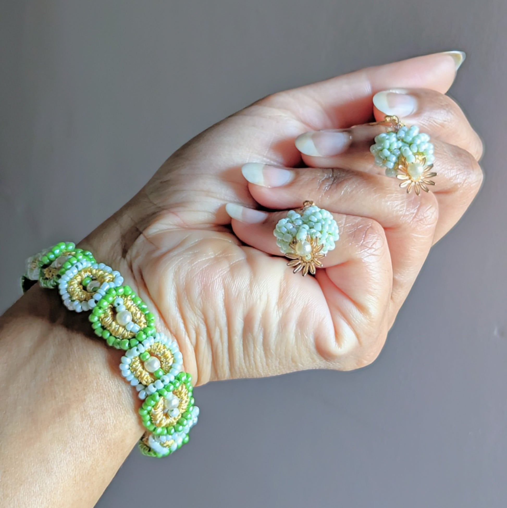 “Hand holding the Pranaya matching jewellery set, featuring a green and pearl beaded bracelet and floral beaded earrings handmade by Mayaani Jewellery UK.”