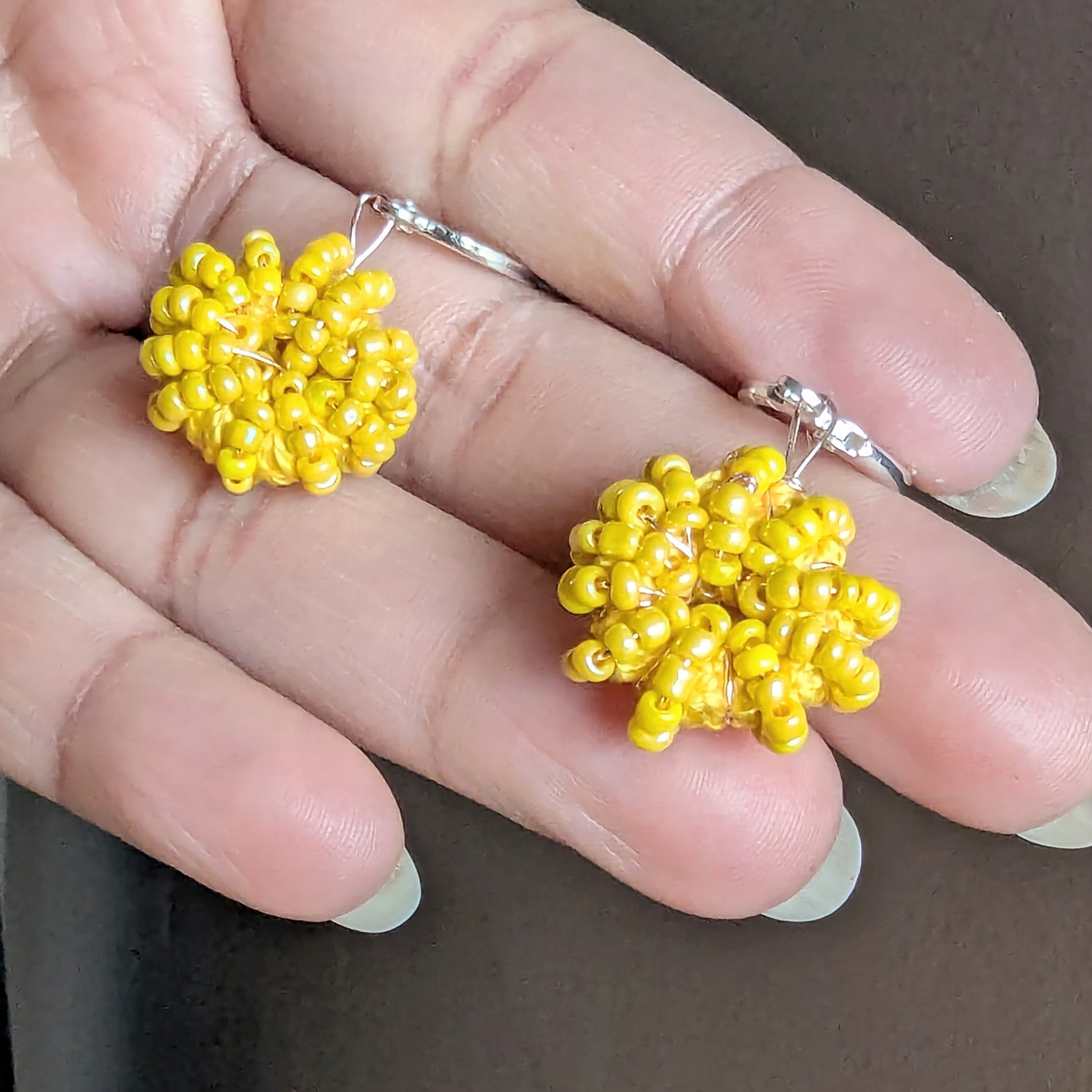 Hand holding a pair of sunflower and lemon yellow beaded hoops handcrafted by Mayaani - close up of beadwork and rose gold plated wire.