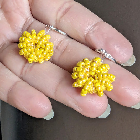 Hand holding a pair of sunflower and lemon yellow beaded hoops handcrafted by Mayaani - close up of beadwork and rose gold plated wire.