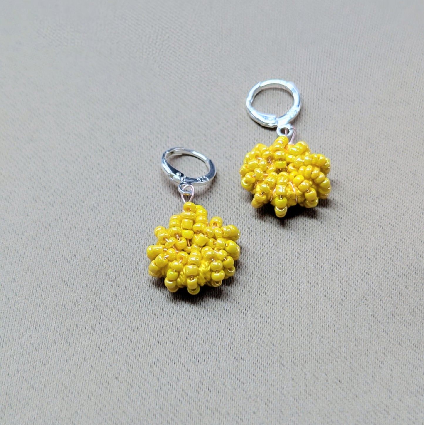 Close up view of a one-of-a-kind hand woven pair of yellow beaded earrings exclusive for everyday by Mayaani Jewellery UK.
