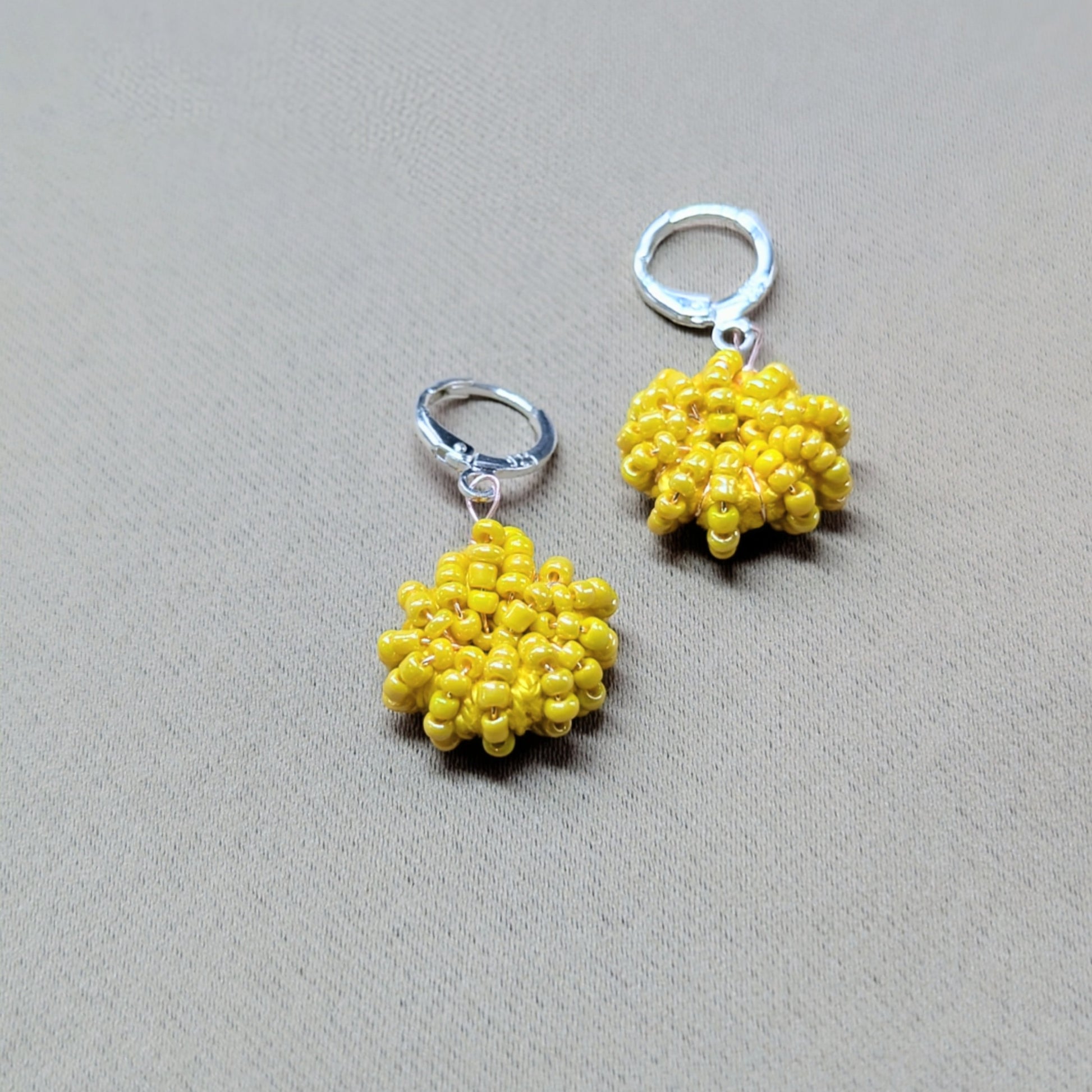 Close up view of a one-of-a-kind hand woven pair of yellow beaded earrings exclusive for everyday by Mayaani Jewellery UK.