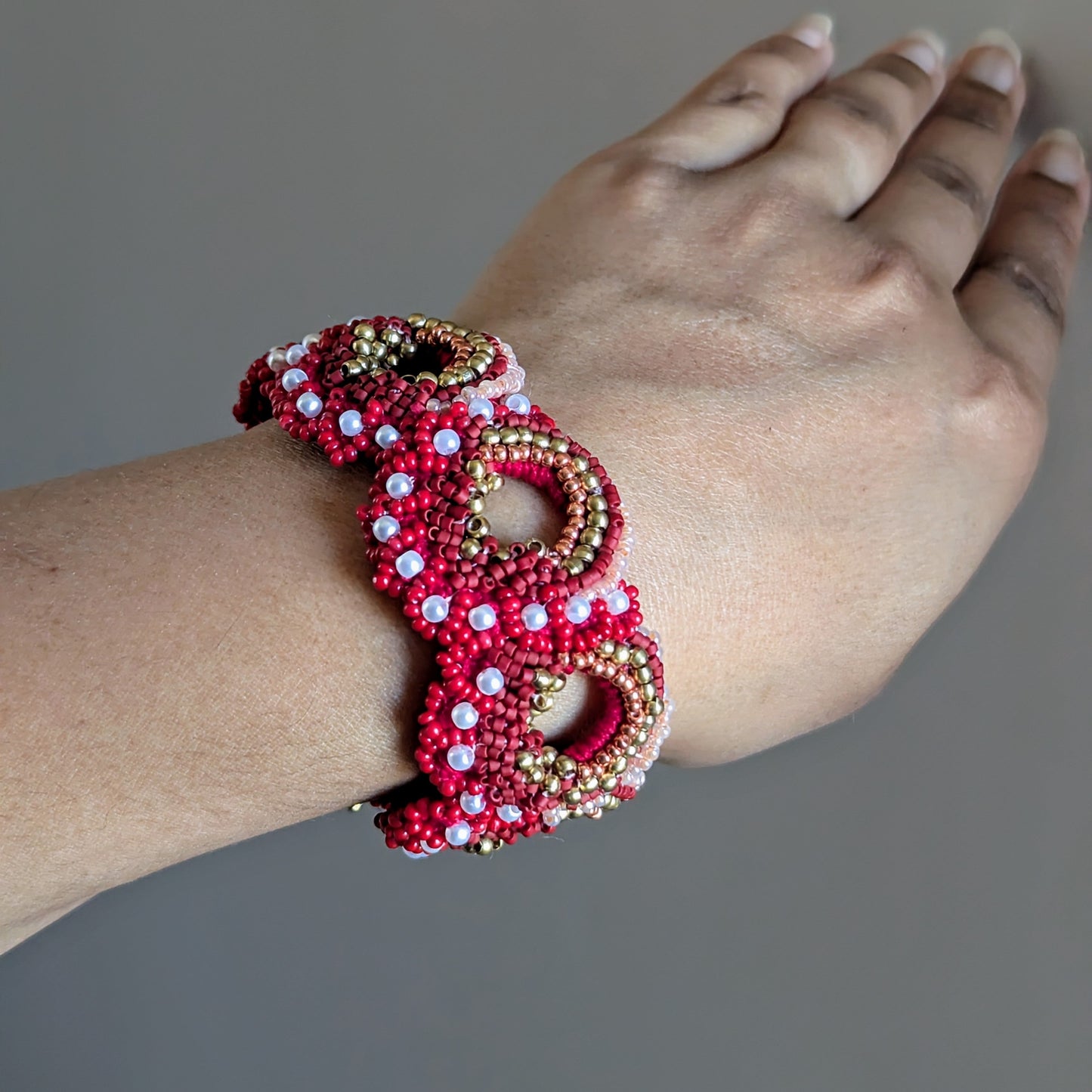 Close up of a wrist modelling the Shreya statement wrist bracelet element in red with gold and pearl accents exclusively handcrafted for Mayaani UK.