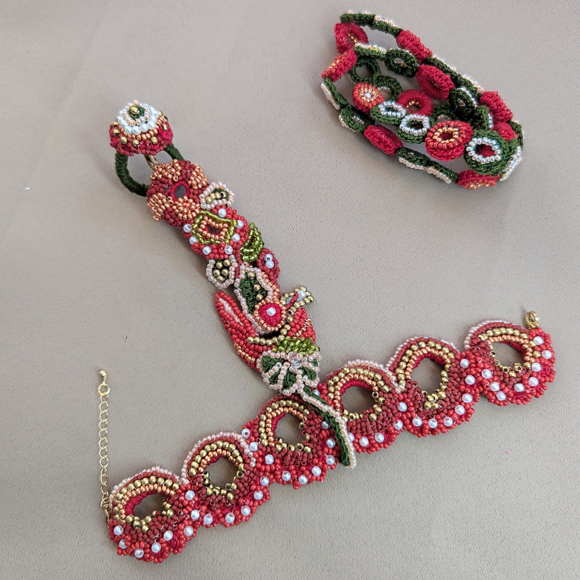 Flat lay of Shreya the 5-in-1 Indian hand bracelet with custom chain in red, gold, green floral motifs exclusive to Mayaani Jewellery UK.