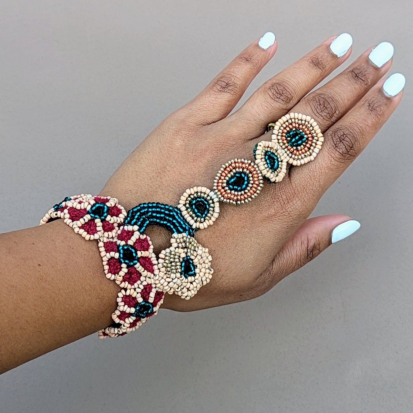 Hand wearing an elegant floral motif bracelet, crafted in emerald green, gold, peach and red tones, a sustainable bridal handmade piece from the Mayaani Jewellery Neha Collection.