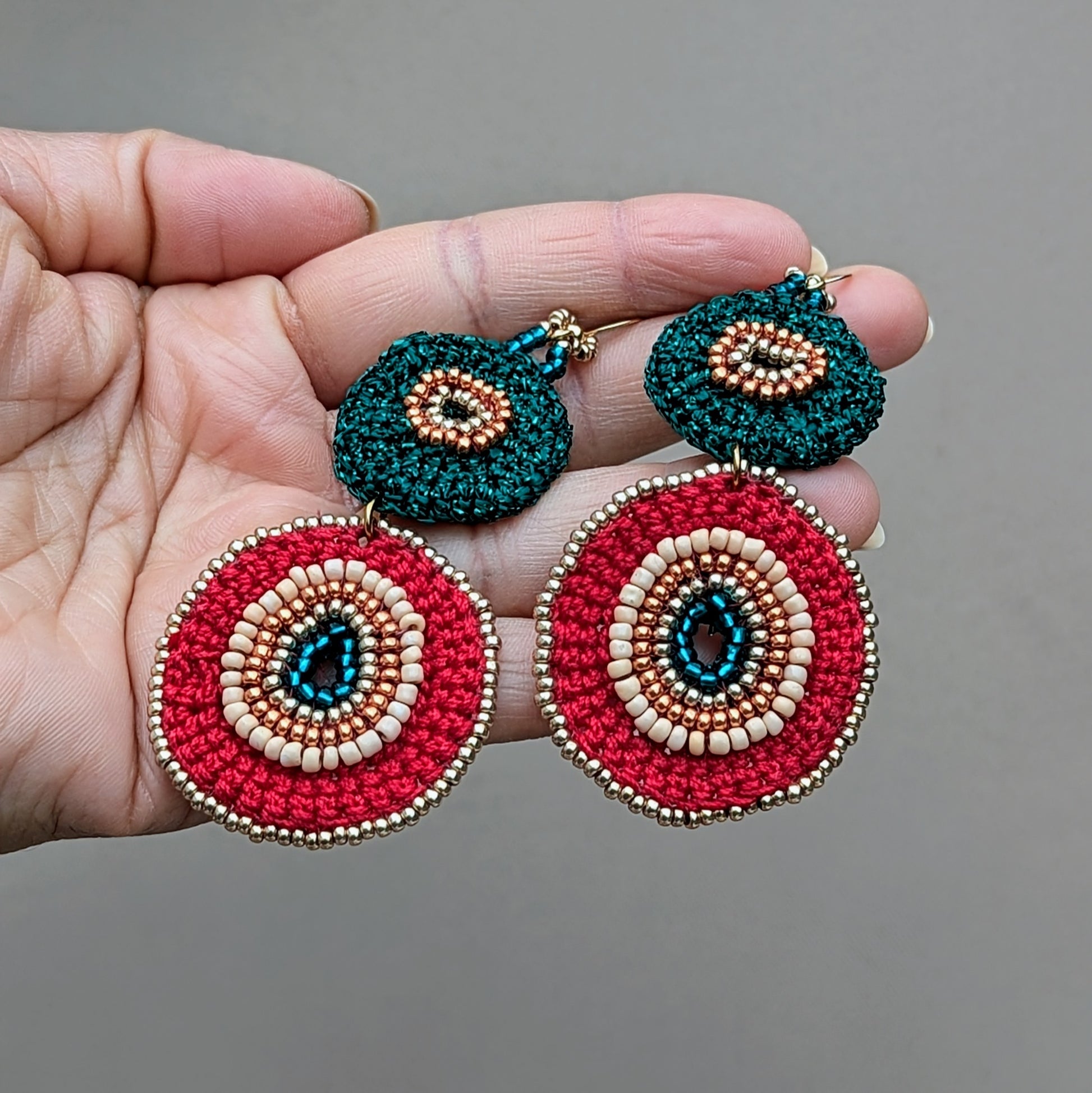 Close up of a bold red, green and gold bead crochet pair of lightweight earrings featuring circular motifs echoing the Indian heritage which inspires all designs at Mayaani Jewellery UK.