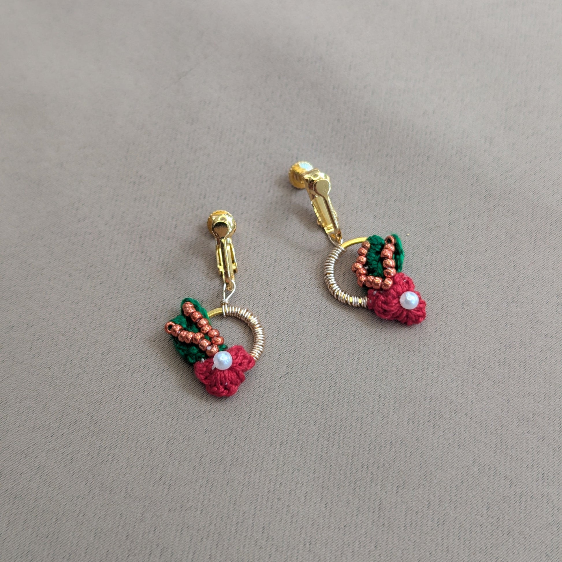 Flat lay view of the red, green, pearl, copper and rose gold Kumkum clip-on earrings designed for premium luxury quality and comfort with sustainability in mind.