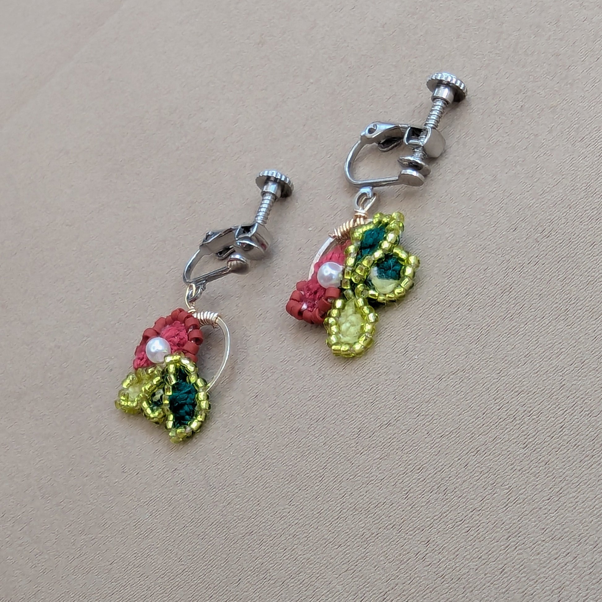 Reva clip-on earring pair separated on neutral surface - showing individual asymmetrical flower design.
