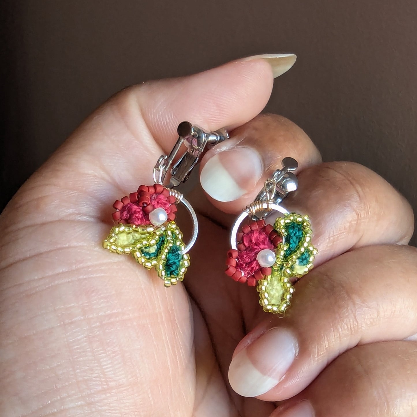 Reva clip-on earrings close-up - deep rose crochet flower with teal and chartreuse seed bead leaf detail.