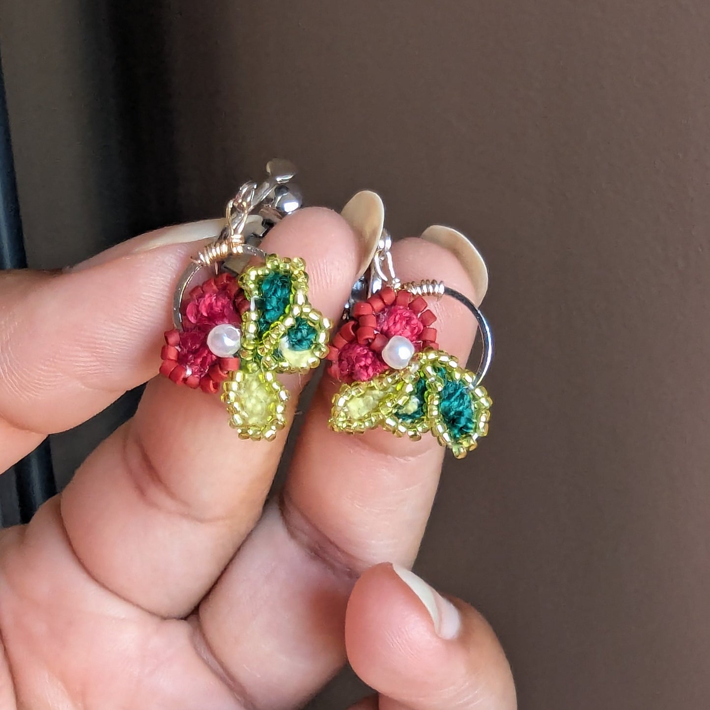 Reva clip-on earrings held in fingertips showing stainless steel screw-back clasp and hoop frame.