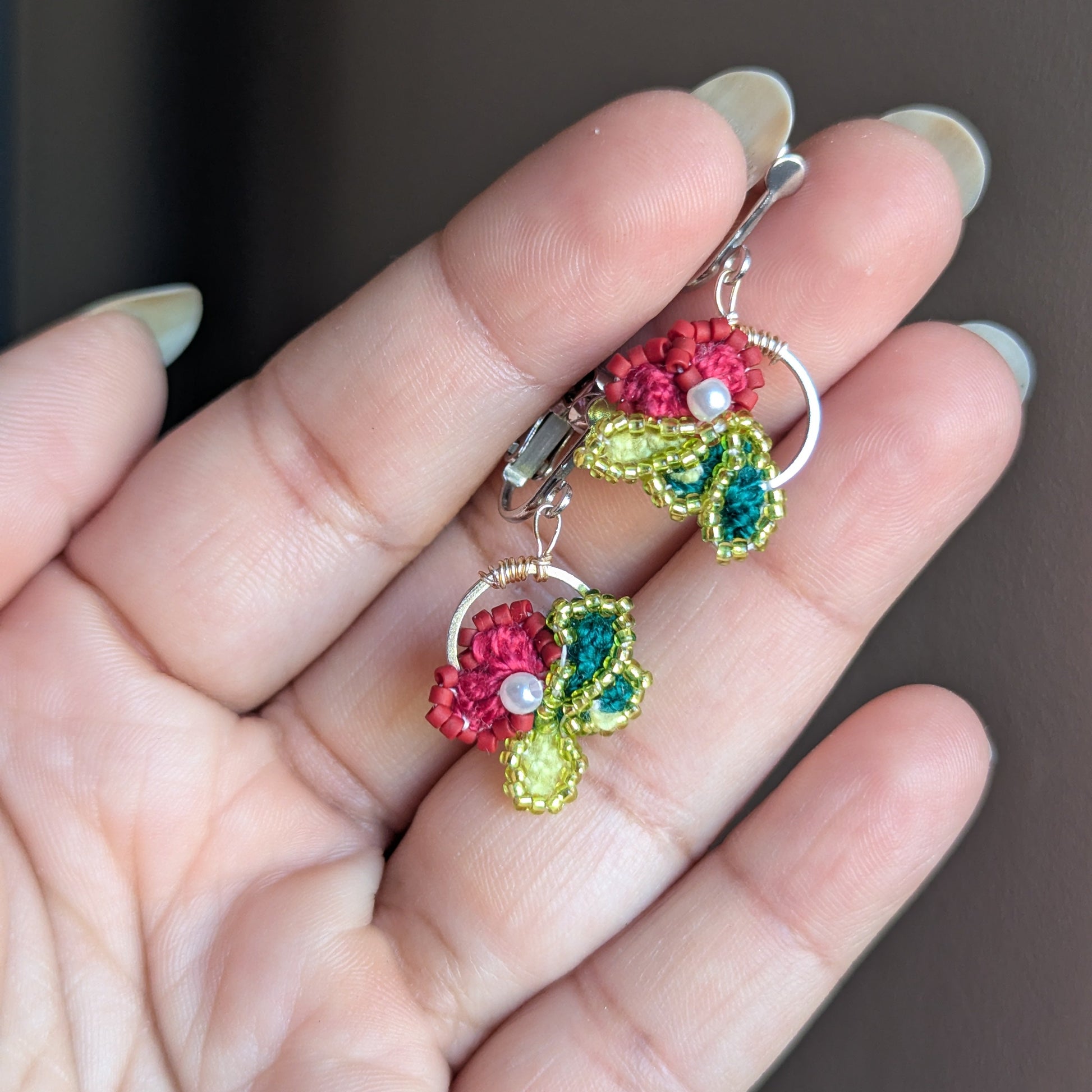 Reva handmade earrings in open palm - rose pink flowers with chartreuse leaf clusters and seed pearl centres.