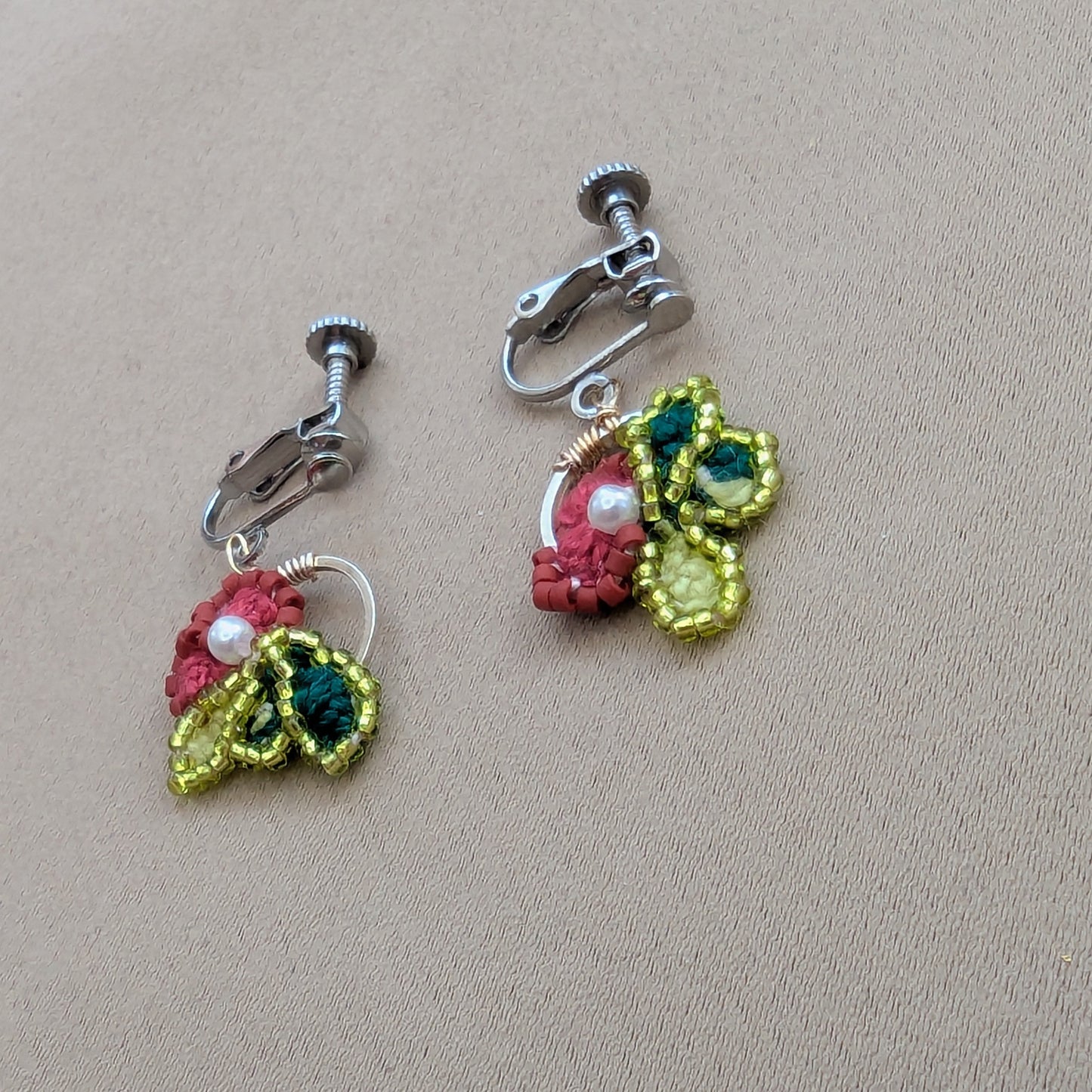 Reva earrings flat lay showing full pair - deep rose flower with chartreuse leaf and pearl centre detail.