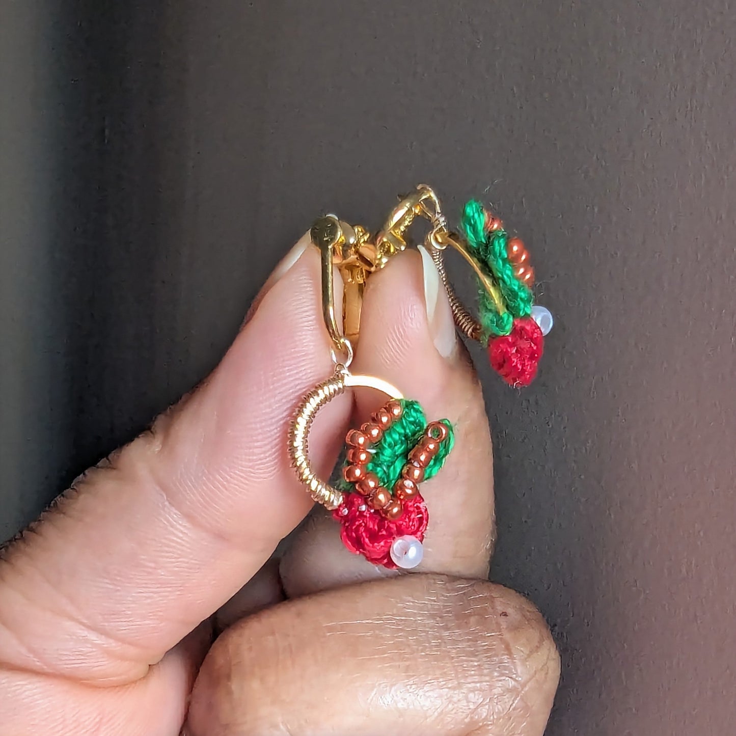 Close up view of a pair of handmade bead woven wire wrapped clip-on Kumkum earrings inspired by botanicals and Indian heritage for comfortable wear for non-pierced ears.