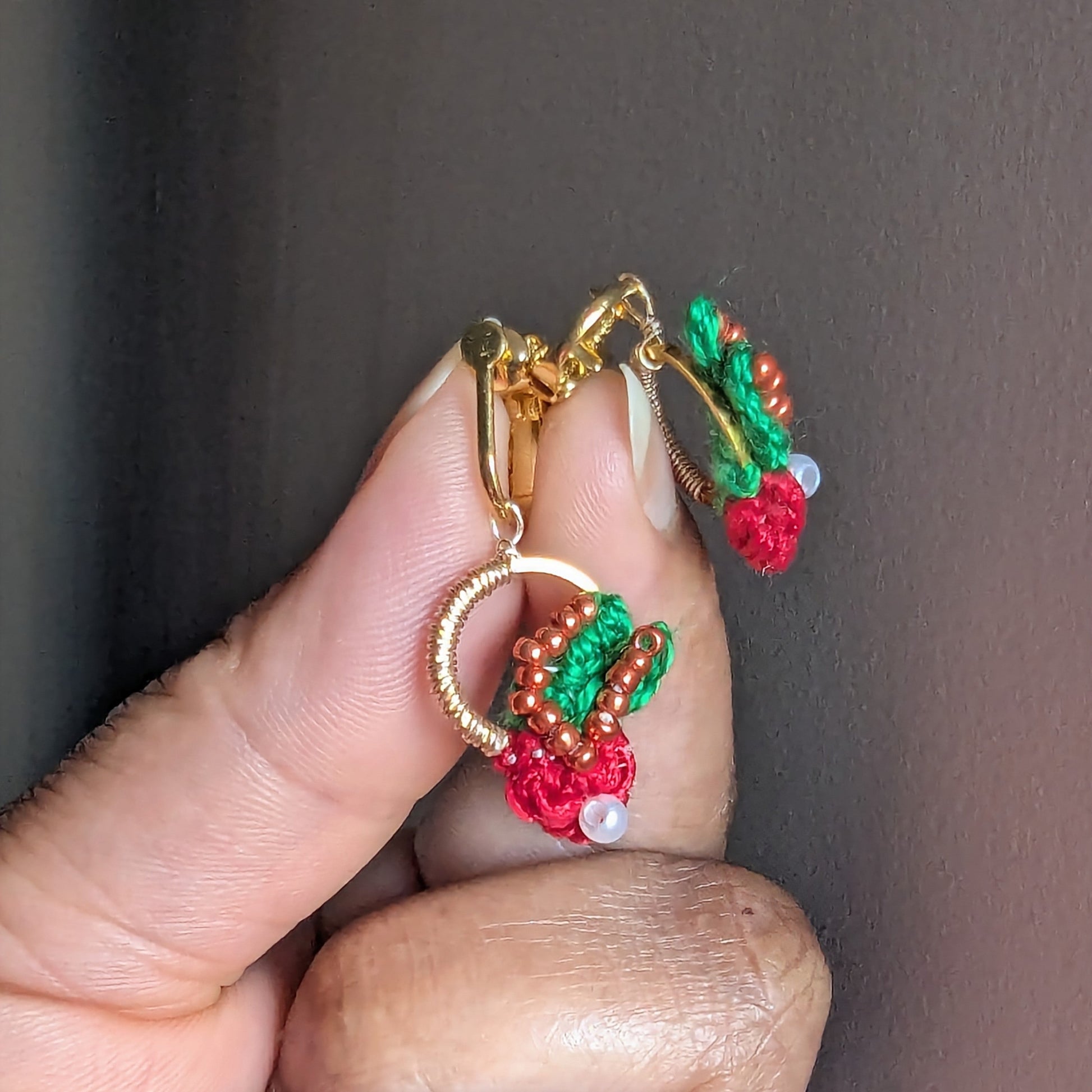 Close up view of a pair of handmade bead woven wire wrapped clip-on Kumkum earrings inspired by botanicals and Indian heritage for comfortable wear for non-pierced ears.