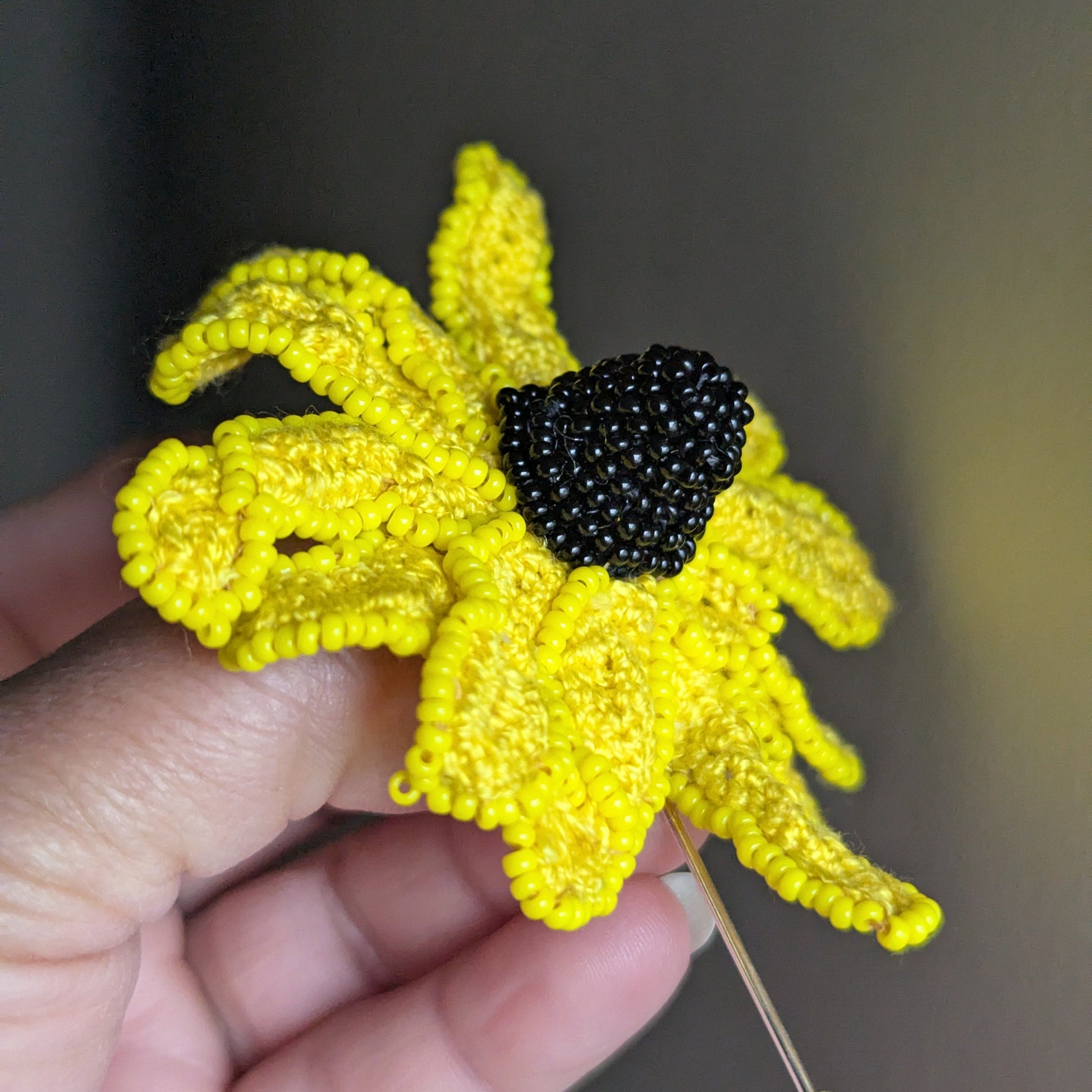 Angled view of the Vamika rudbeckia brooch pin showcasing the sculptural black seed bead centre and textured yellow petals.