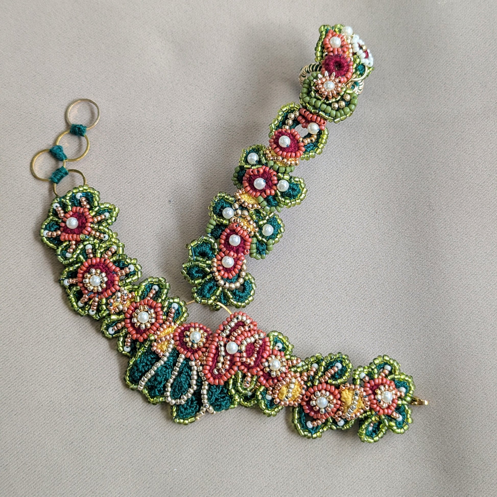 Flat lay close up view of the Rukmini 5-in-1 Indian hand bracelet artisan made exclusively for Mayaani Jewellery in emerald green, olive green, gold, yellow, red and pearl tones.
