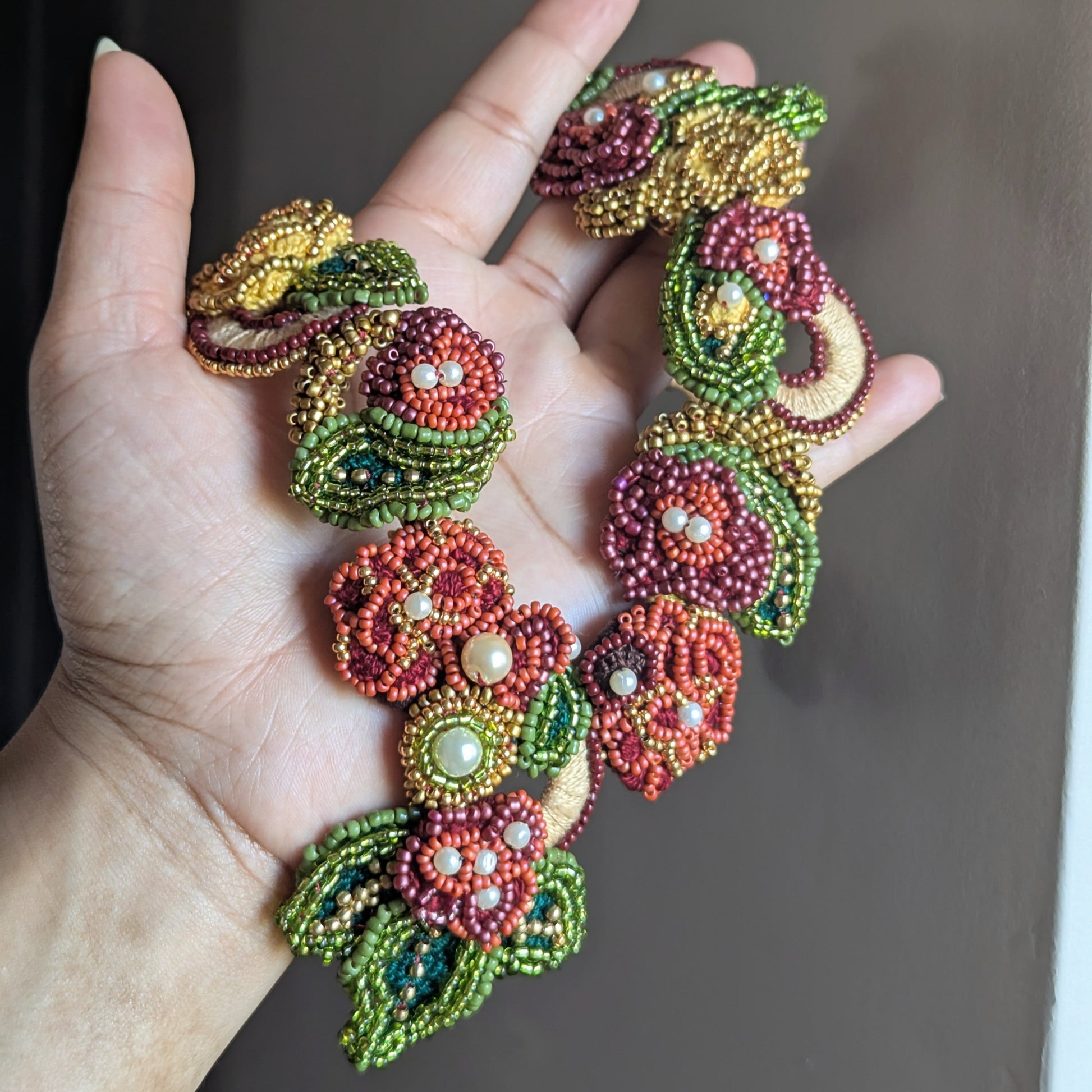 Detailed view of the Rukmini 2-in-1 Indian inspired statement couture necklace exclusive to Mayaani Jewellery. Pictured held in hand featuring reds, greens, golds, yellow and soft pearl accents.