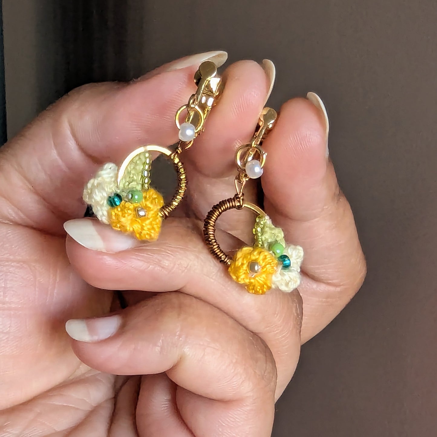 Close up view of a one off couture pair of heirloom quality Sauri clip-on earrings by Mayaani Jewellery UK inspired by Indian heritage and floral accents in yellow, cream, bronze, gold, pearl and green.