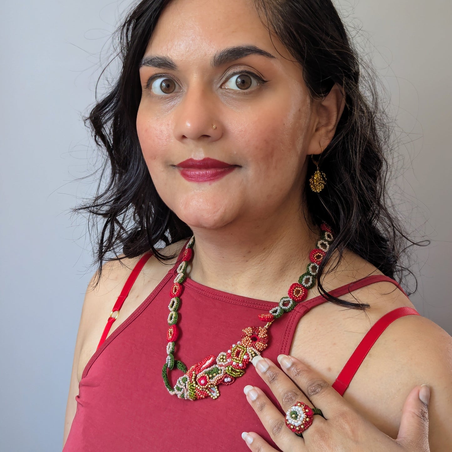 Close up view of Megha of Mayaani Jewellery modelling the ring and necklace elements of the Shreya 5-in-1 red, gold and green Indian hand bracelet exclusively handcrafted in the UK.