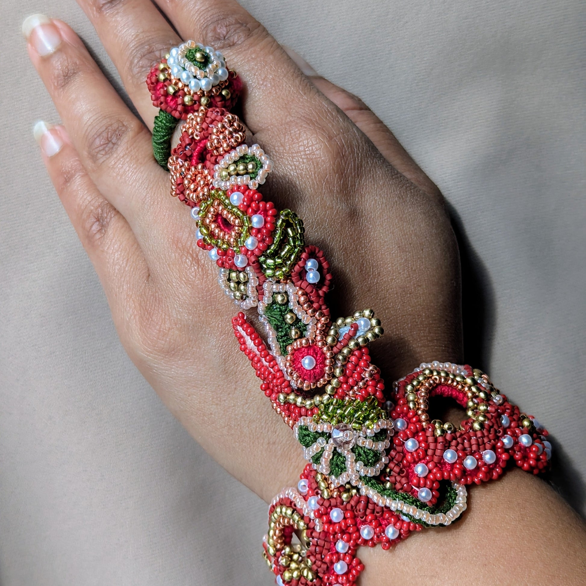 Close up of a hand modelling the Shreya 5-in-1 Indian hand bracelet in traditional Indian bridal colours.