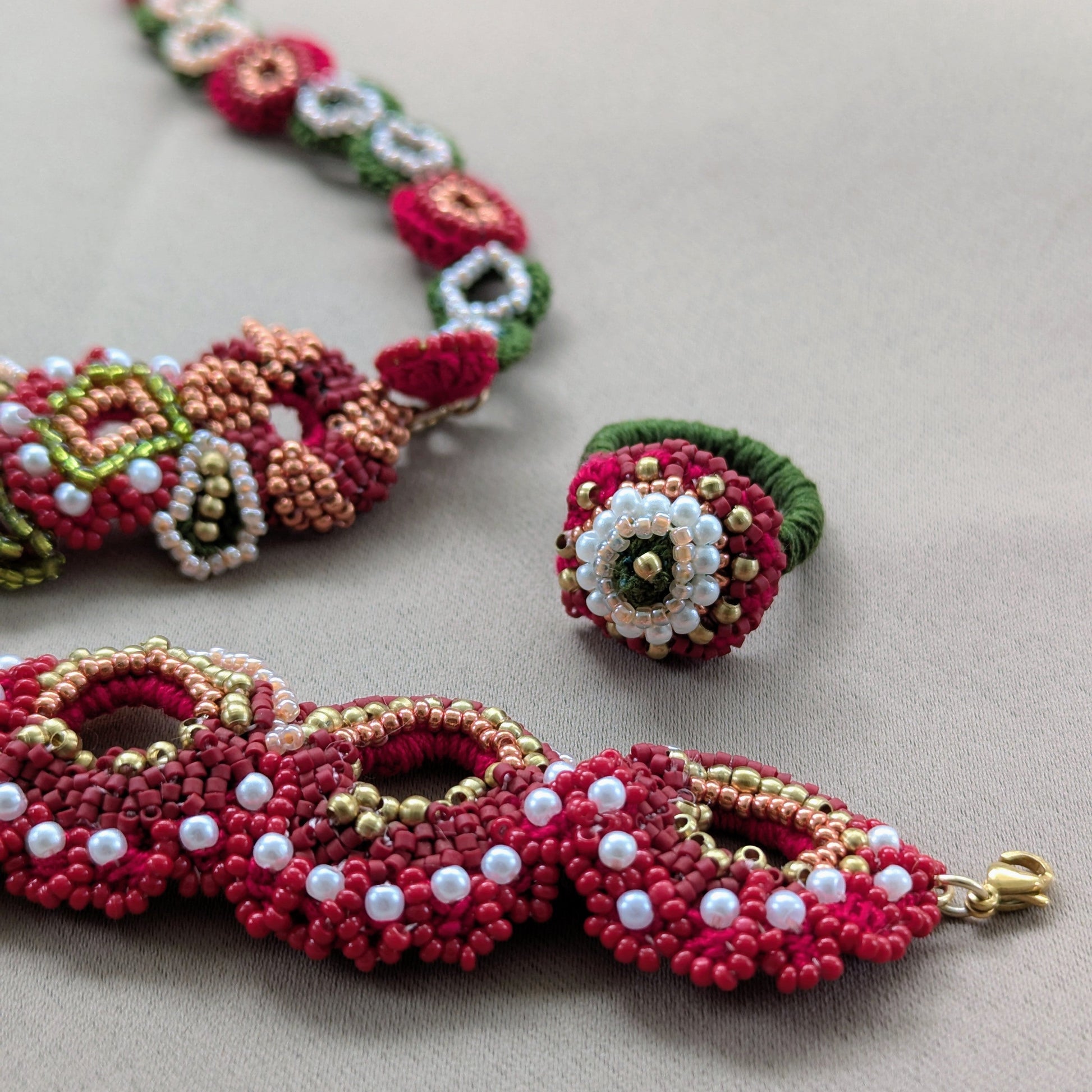 Close up detailed view of the Shreya 5-in-1 ring, bracelet and necklace elements featuring richly layered red glass seed beads, solid gold brass beads and ivory pearl seed beads.