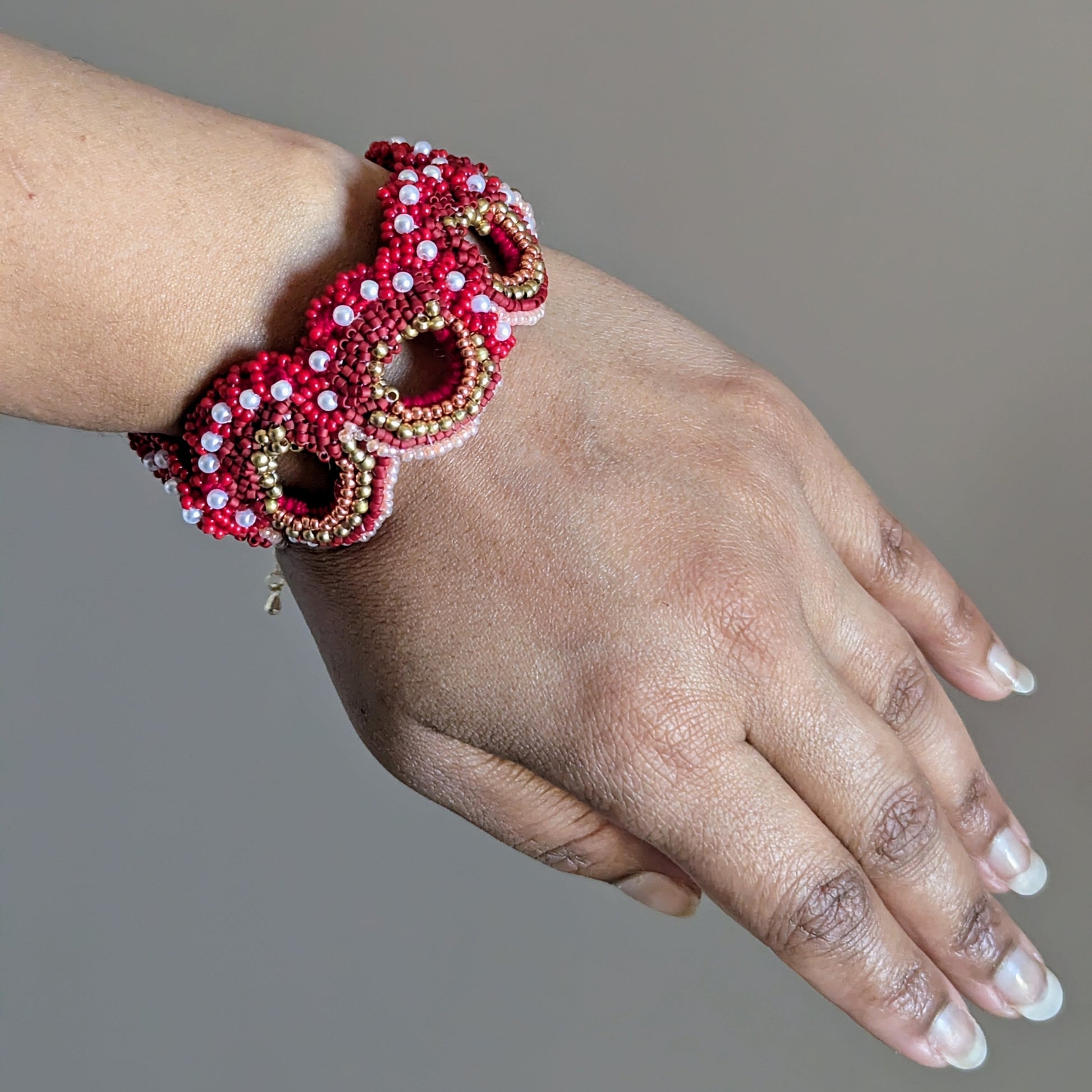 Close up of a person's wrist wearing the Shreya red designer Indian artisan made bracelet with gold and pearl accents. Made in the UK.