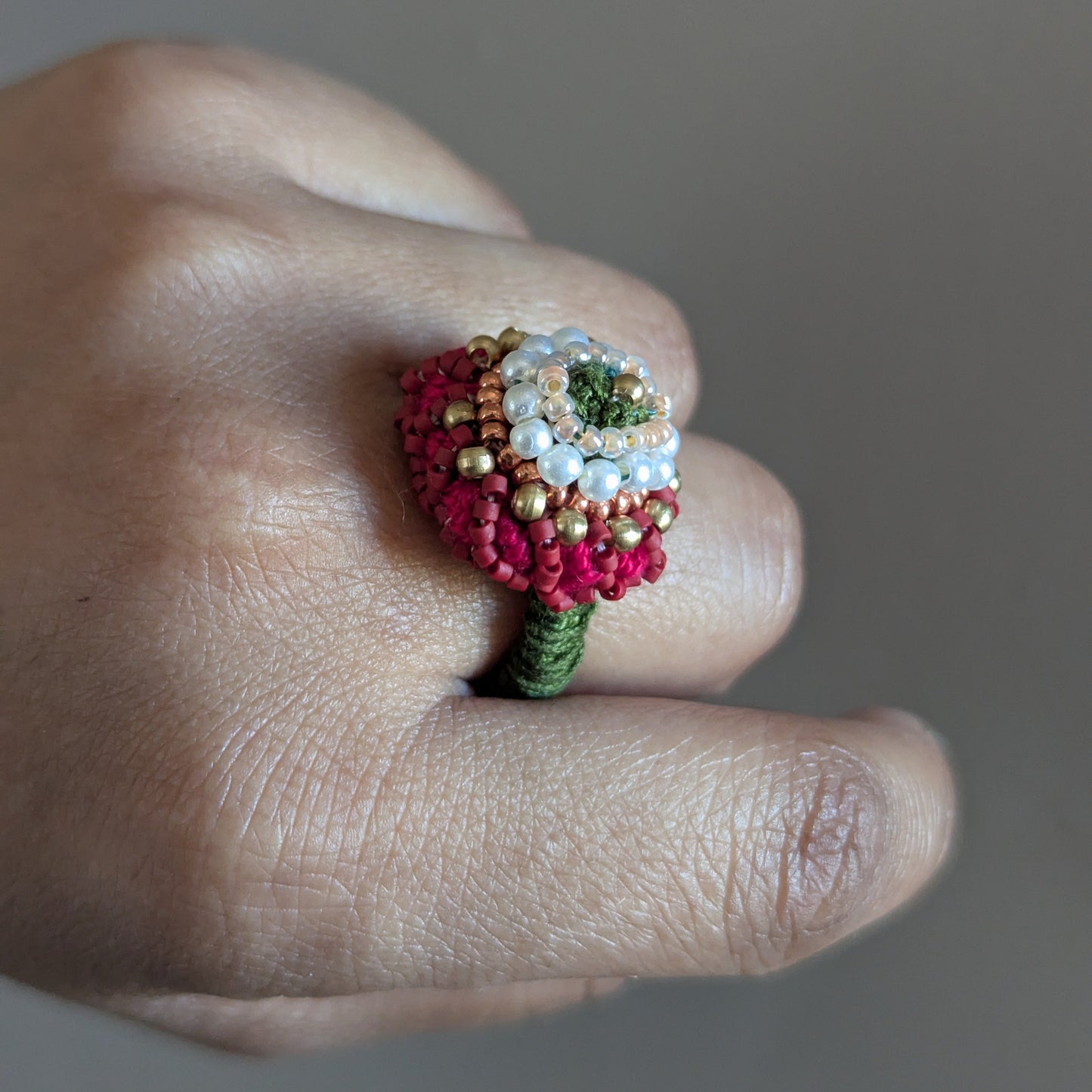Close up of a hand wearing the Shreya 5-in-1 ring element in solid brass, seed pearl and red seed beads featuring hand bead work and crochet.
