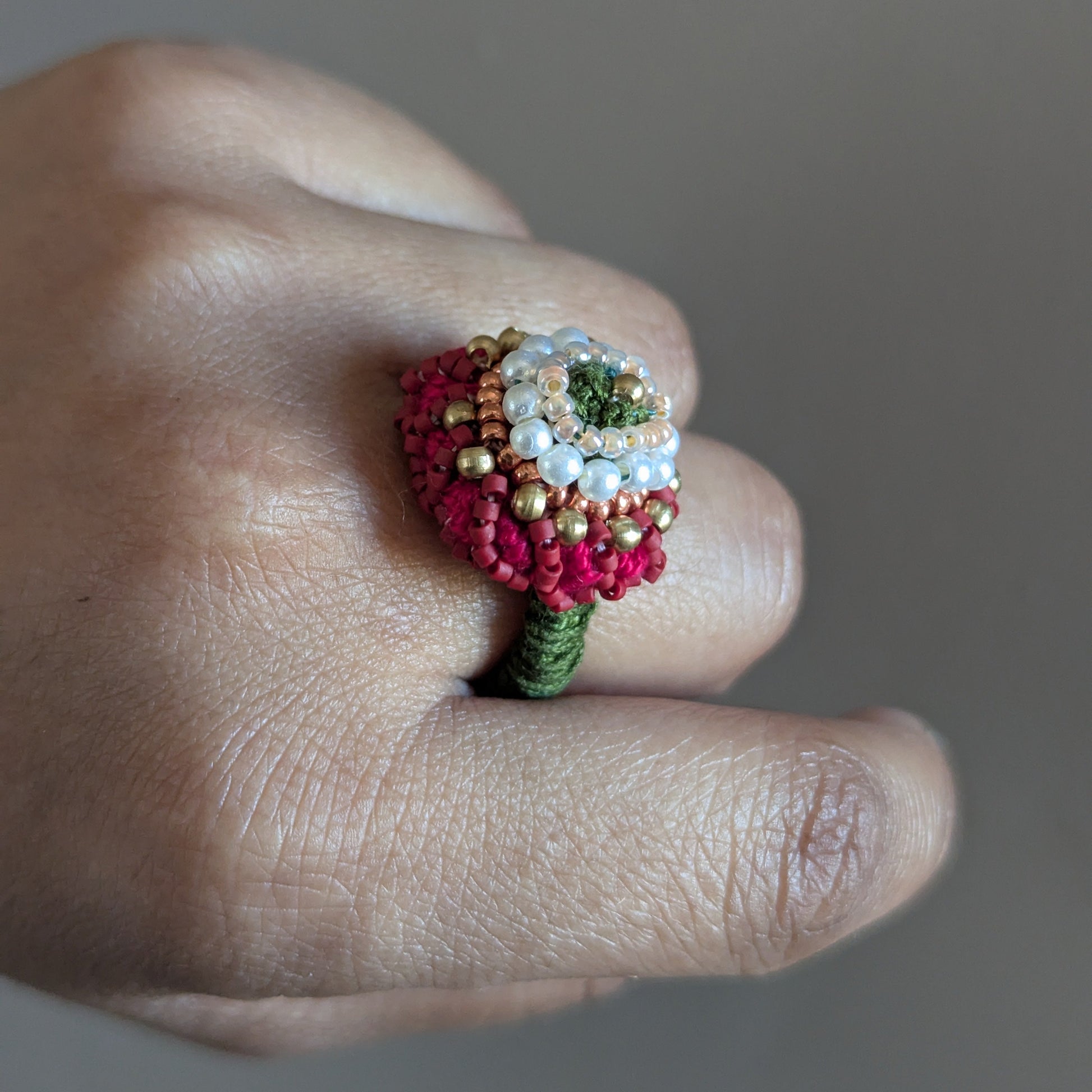 Close up of a hand wearing the Shreya 5-in-1 ring element in solid brass, seed pearl and red seed beads featuring hand bead work and crochet.
