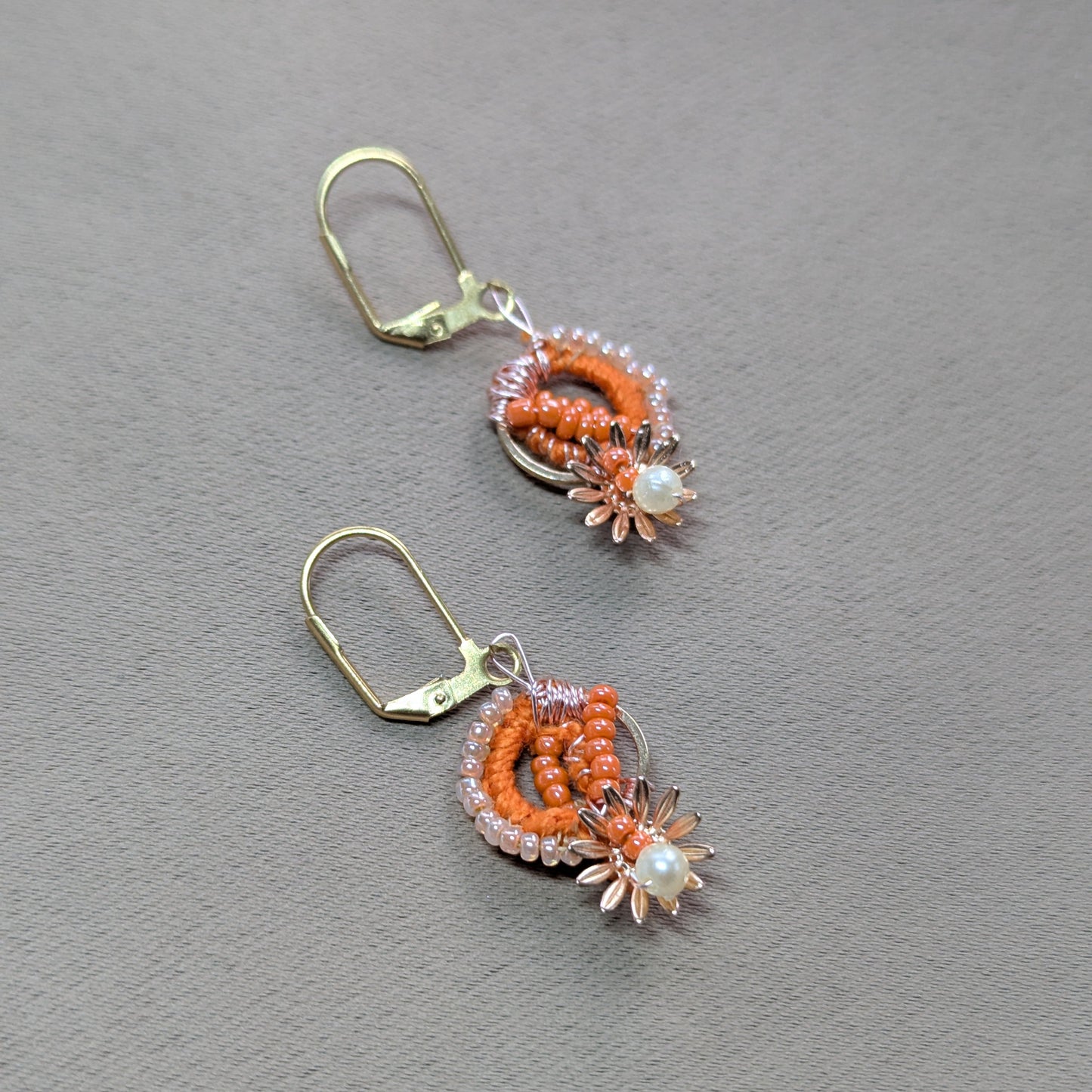 One-of-a-kind orange and gold Indian beaded earrings displayed in hand.