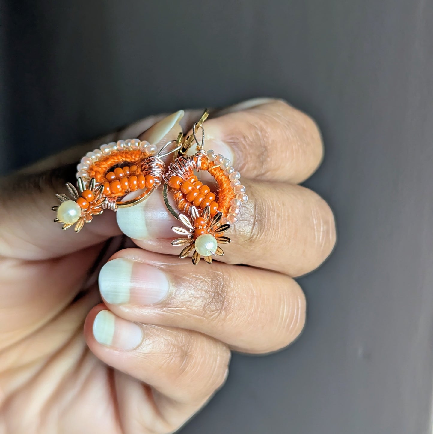 Hand holding Suhasani orange and gold handmade Indian earrings with bead embroidery exclusive to Mayaani.