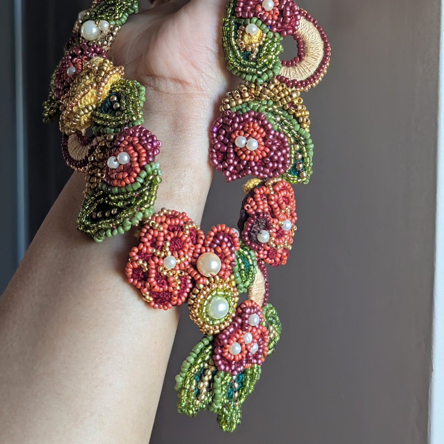 Colourful modern Indian fusion bead woven necklace unique to Mayaani Jewellery UK pictured held in hand displayed against a neutral backdrop.