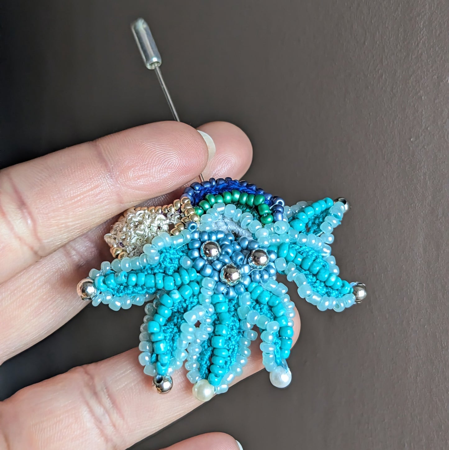 Front view of Jalika artisan beaded brooch in turquoise tones with Czech glass beads, silver accent beads and pearl cotton embroidery.