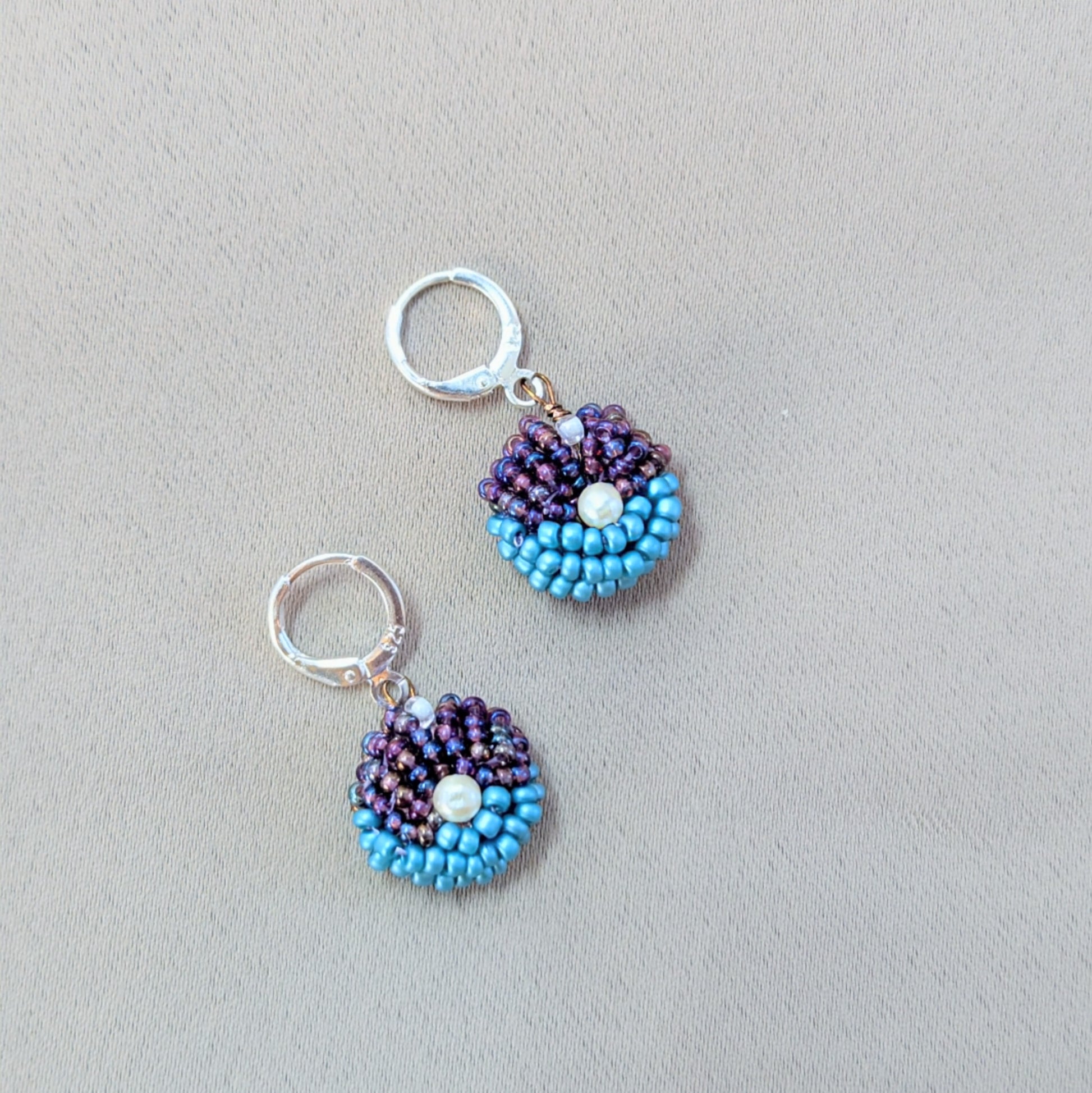 Pair of purple and blue beaded earrings displayed on neutral background showing handcrafted texture and shine.
