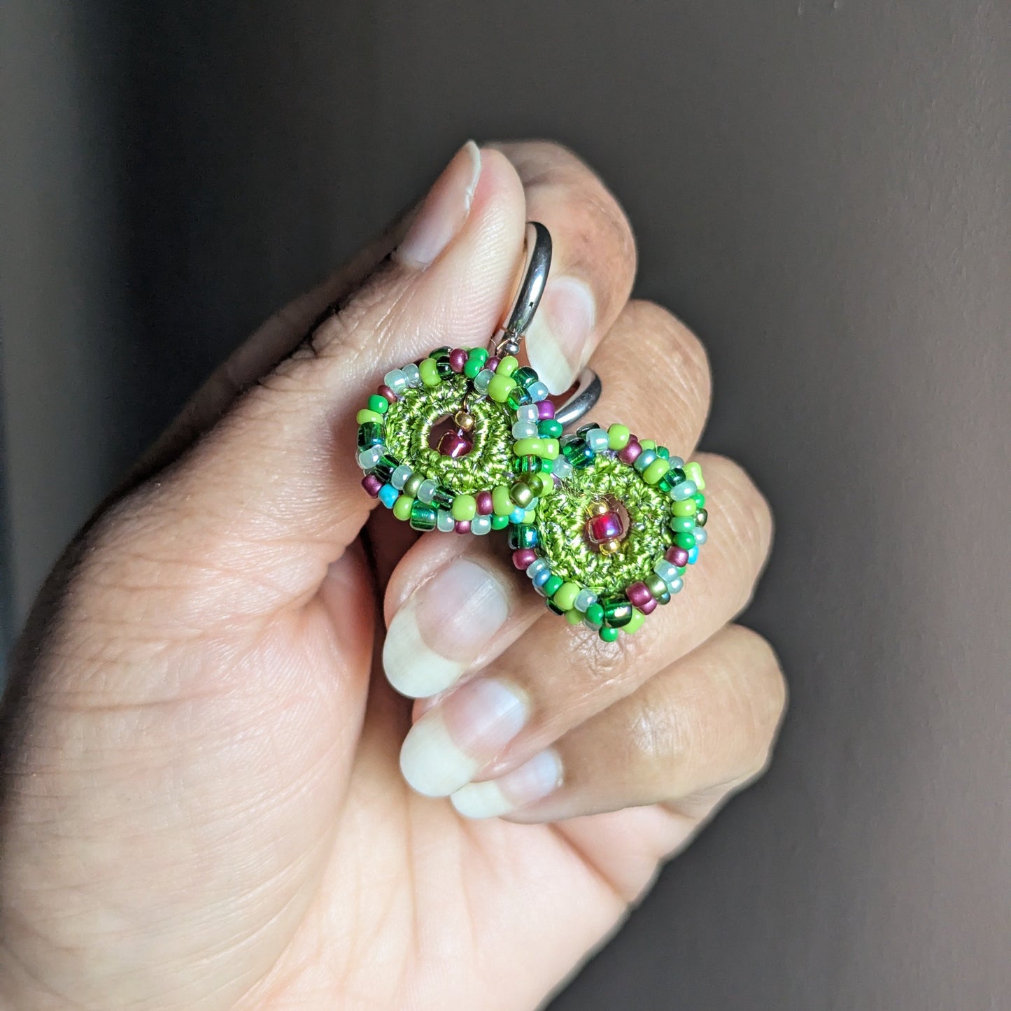 Vana beaded earrings held in hand, focussing on circular crochet centres, multicolour seed bead edging, and sustainable handmade craftsmanship.