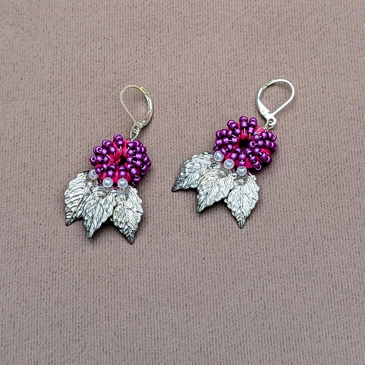 Purple and silver leaf earrings handcrafted with crochet and seed bead detailing on neutral fabric backdrop.