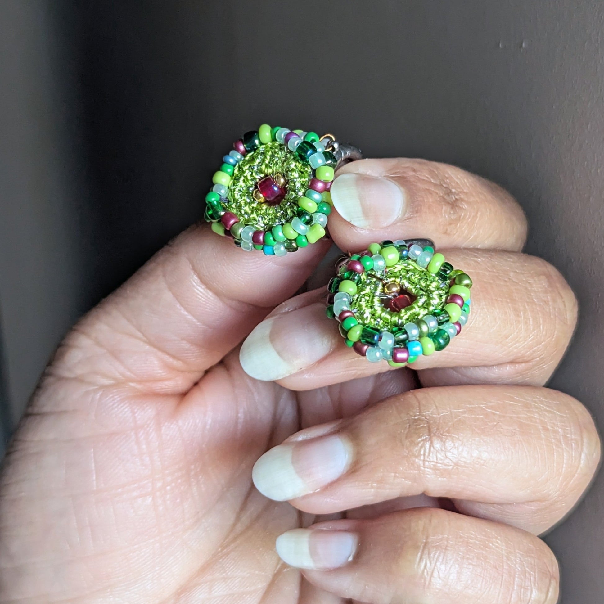 Pair of Vana artisan earrings held individually in hand, highlighting symmetry, colour variation, and the handcrafted nature of each circular bead crochet piece.