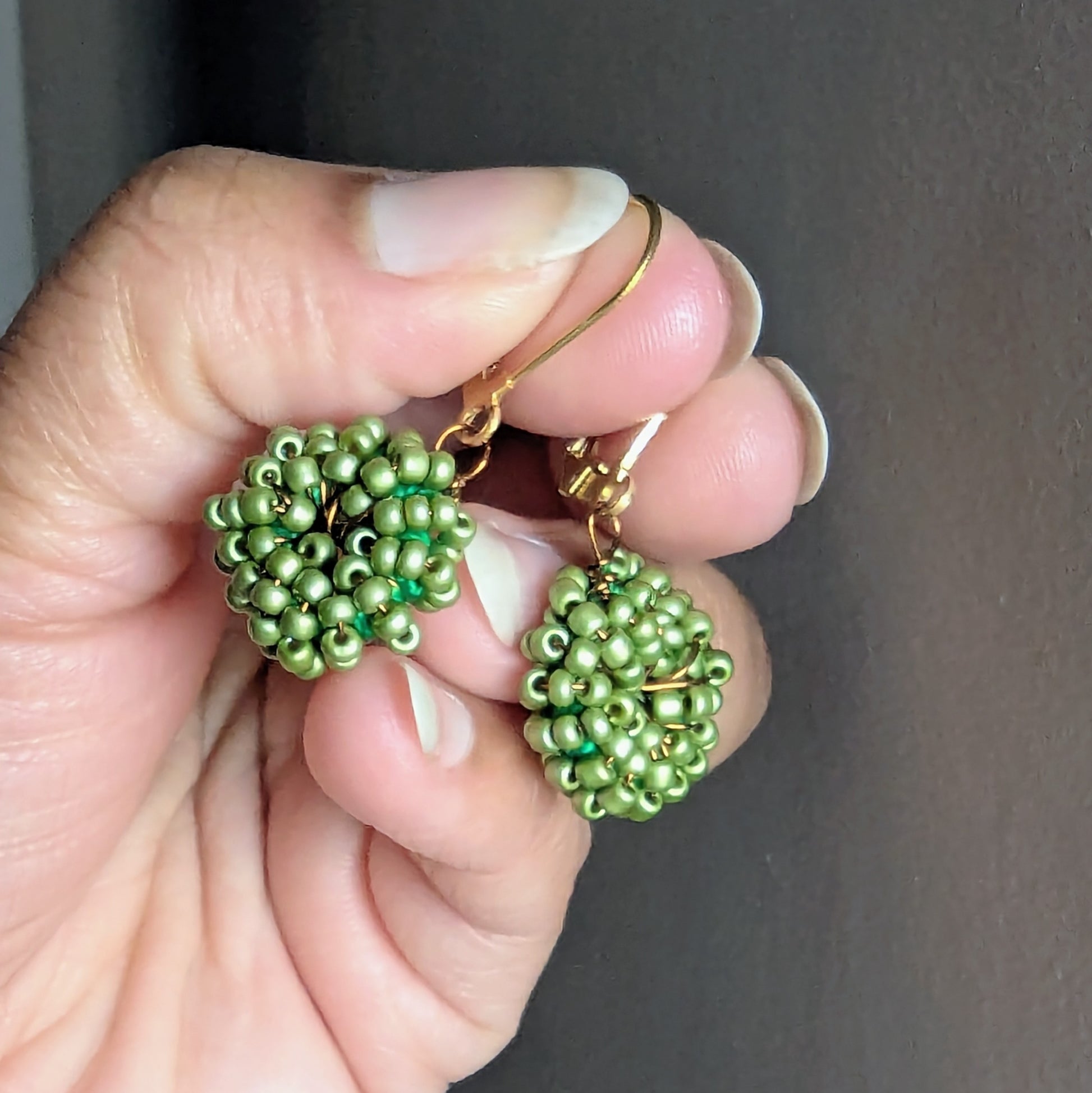 Hand holding soft green hand beaded earrings against a neutral background