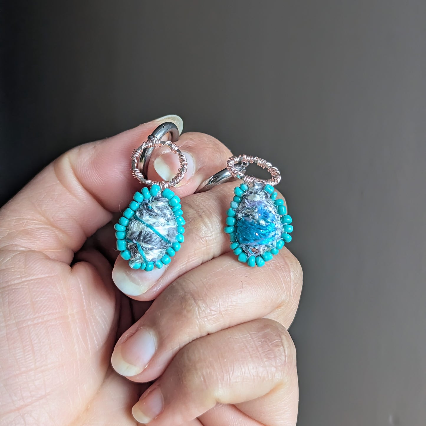 Tarini asymmetric scrap bead earrings with turquoise glass seed bead border held in hand, handmade sustainable jewellery UK.