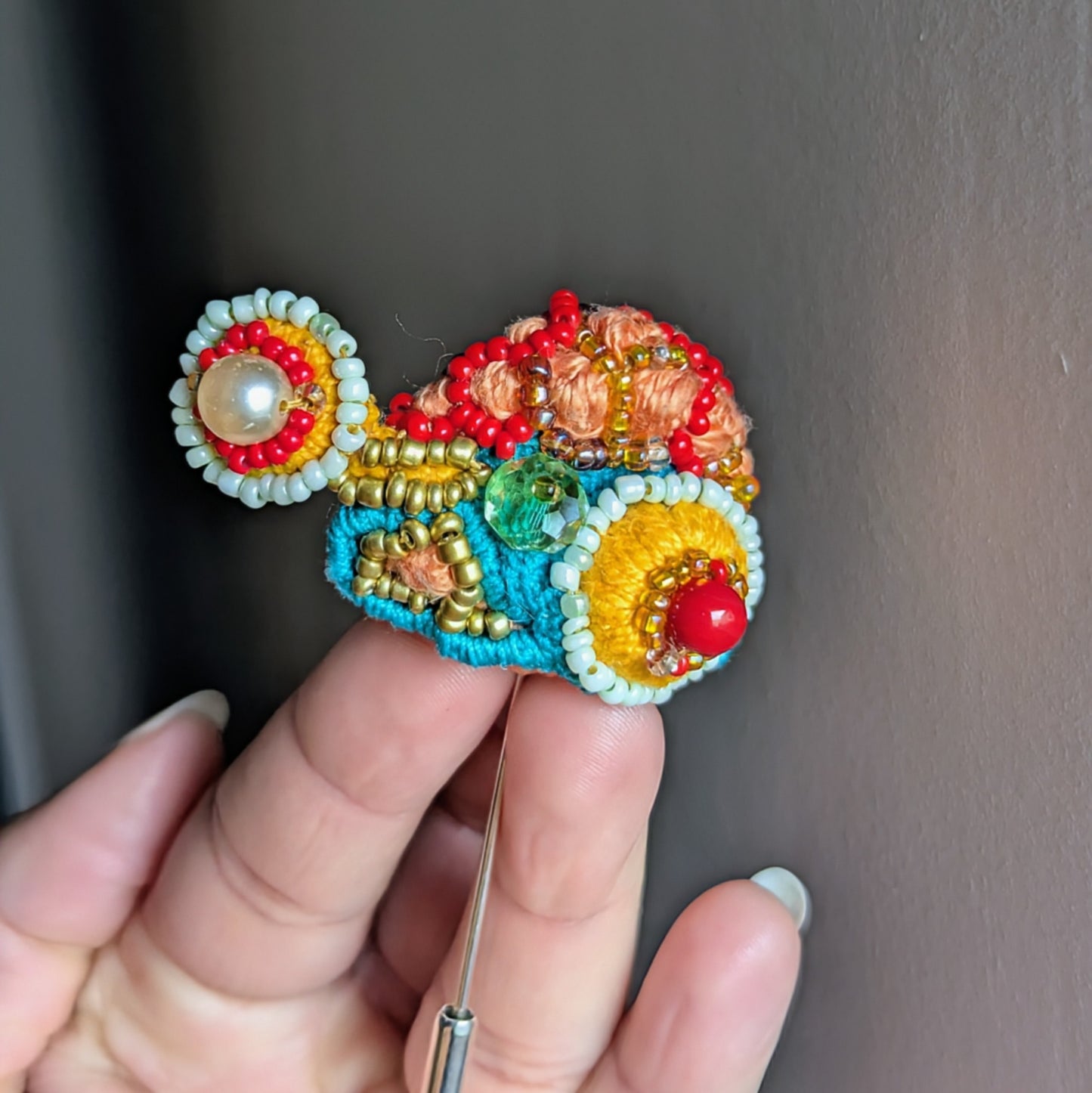 Tejasi colourful beaded brooch showing in hand for scale with vintage seed pearls, Czech glass beads and triple mercerised cotton threads.