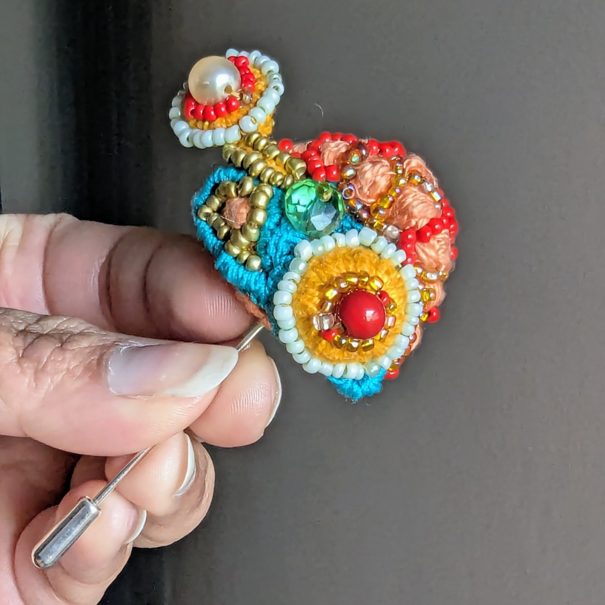 Tejasi handmade orange, blue and red beaded statement brooch held in hand, featuring vintage crystal glass beads, seed pearls and layered textile embroidery. 