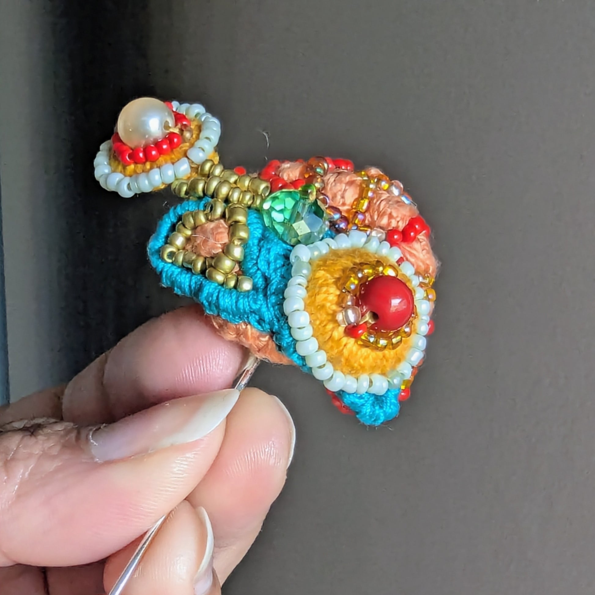 Angled view of Tejasi colourful statement brooch showing sculptural beadwork, vintage green crystal and triple mercerised cotton threads.