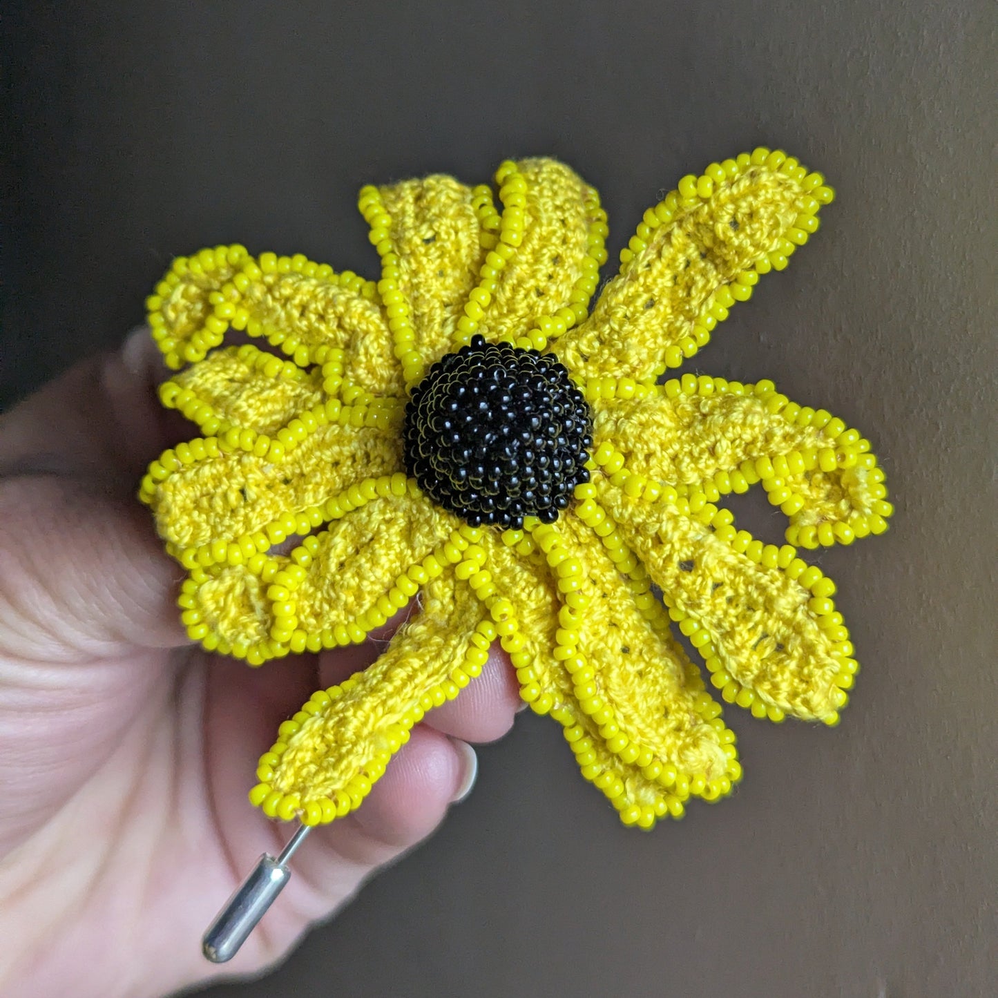 Vamika handmade rudbeckia flower brooch by Mayaani Jewellery -sunshine yellow crochet petals with black seed bead centre held against a grey backdrop.