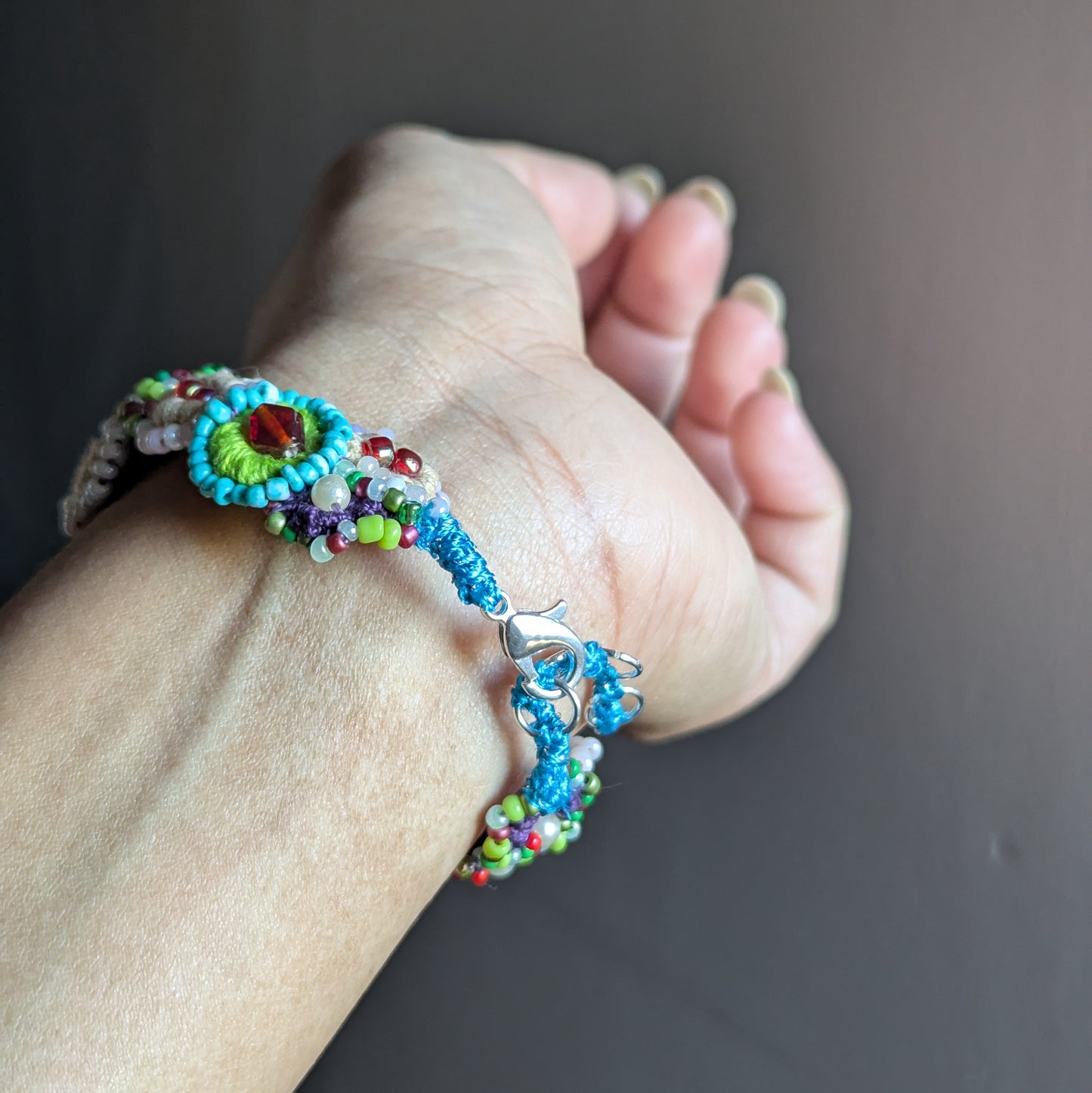 Side view of a handmade beaded bracelet on the wrist, showing layered circular beadwork, stainless steel rings, and a silver-plated lobster clasp.